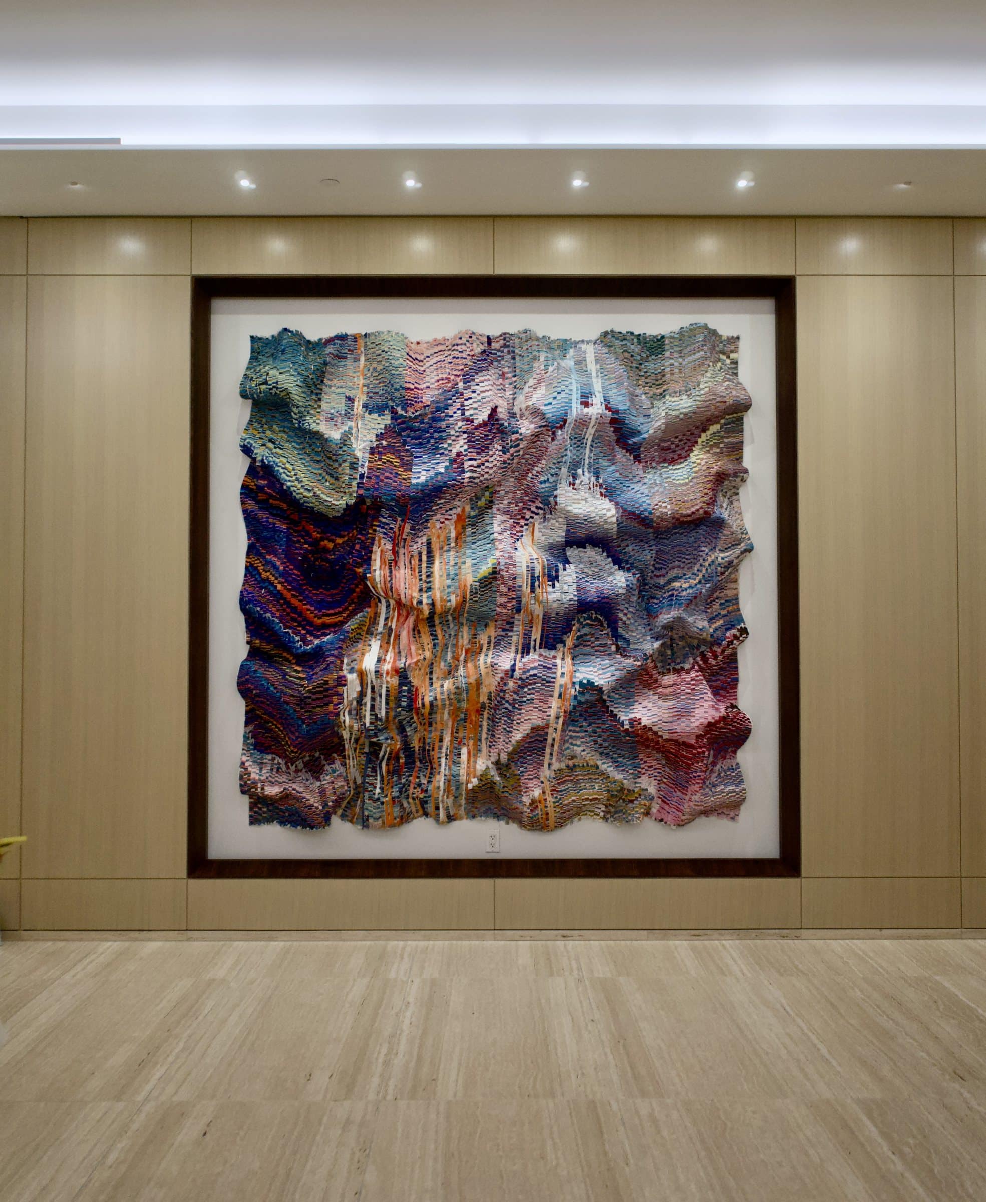 Close frontal view of the pink, lavender, blue and orange cut-silk work mounted inside a dark wall frame