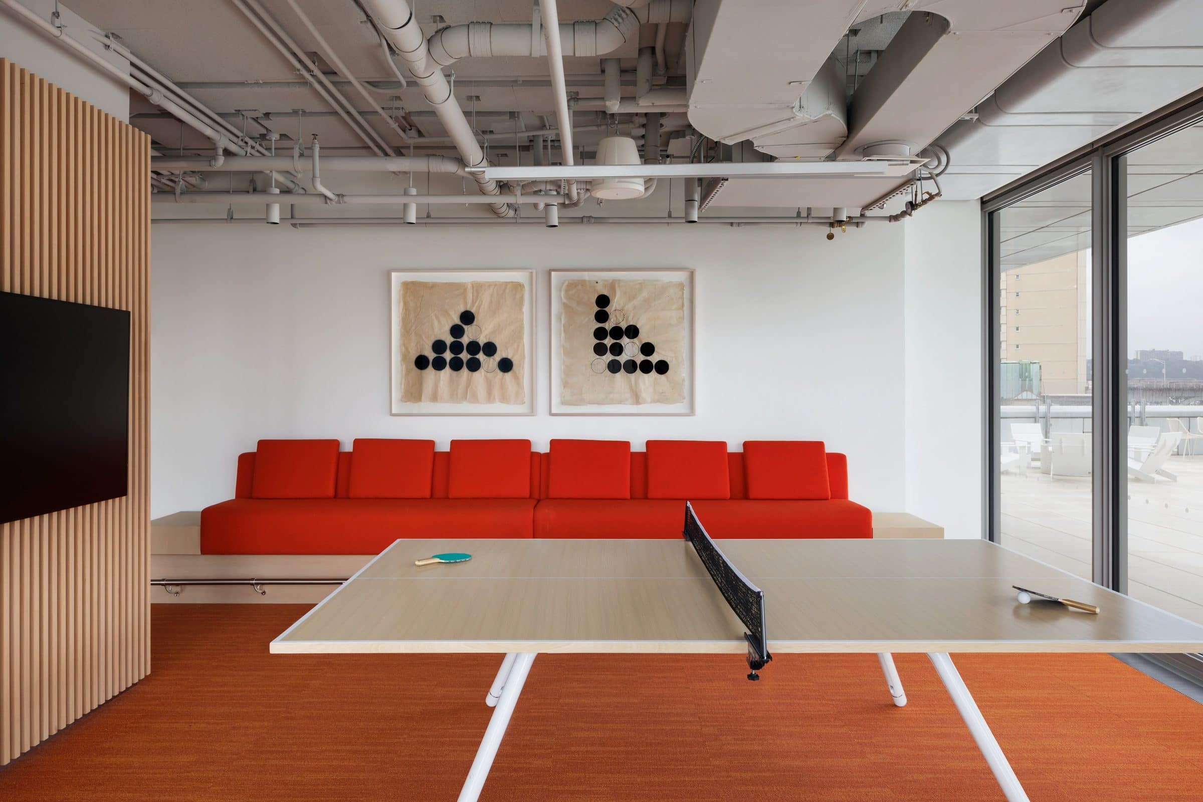 Two framed works of black dots arranged in triangles on handmade paper above a red banquette and a ping-pong table