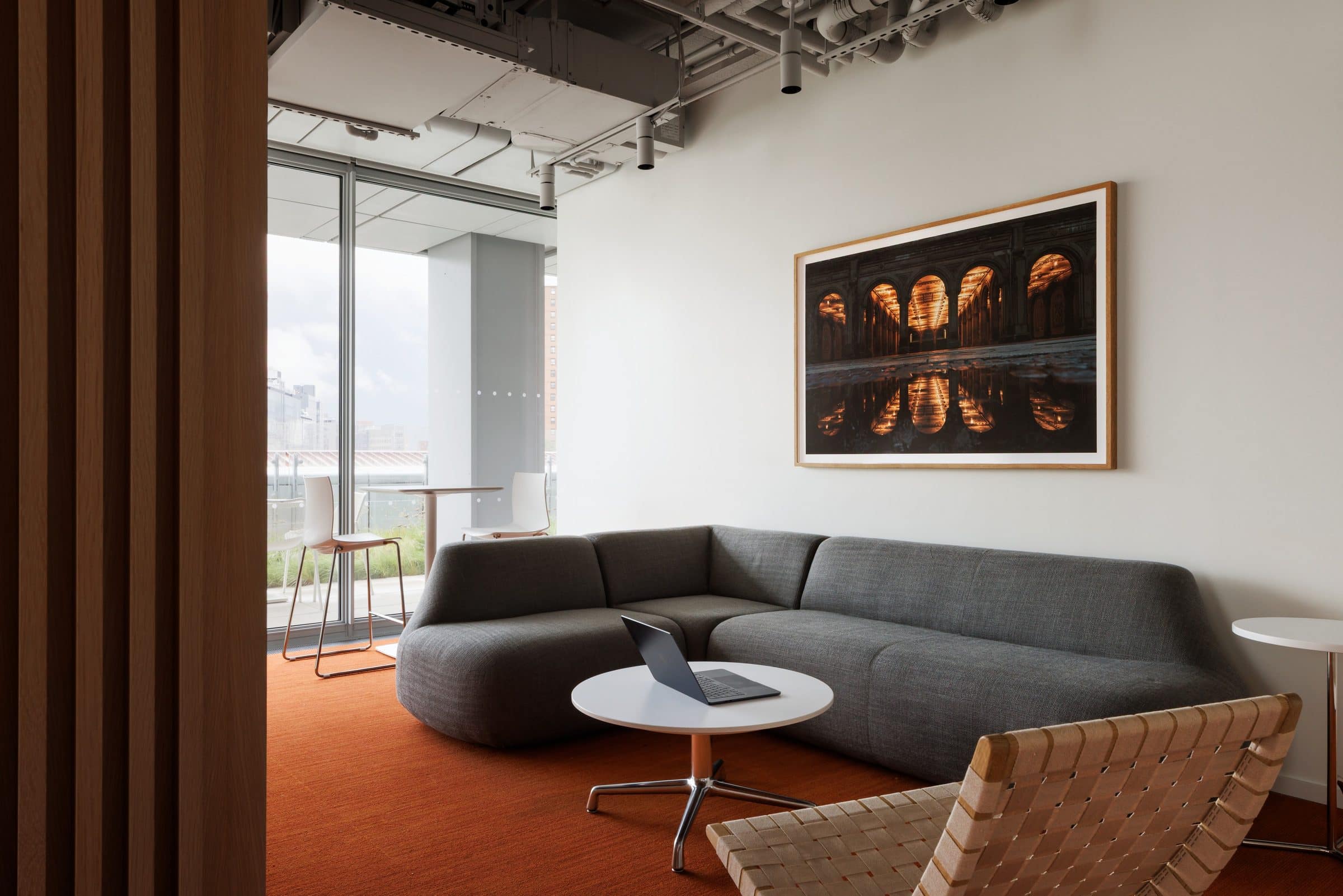 Large photograph of lit arches reflected in water above a gray sectional sofa beside a window to a terrace