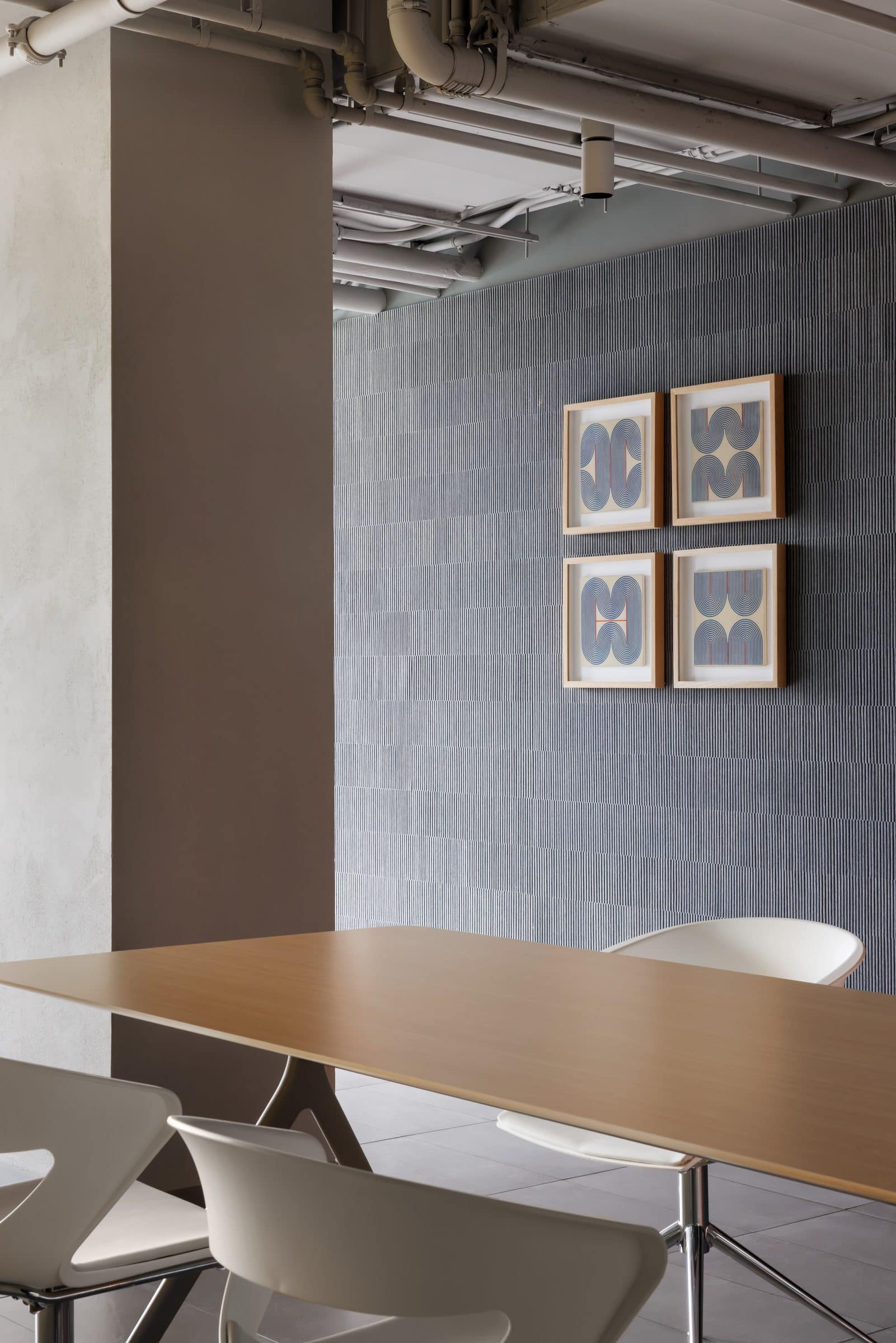 Four framed ceramic tiles with blue looping line patterns on a textured gray wall beyond a wooden table