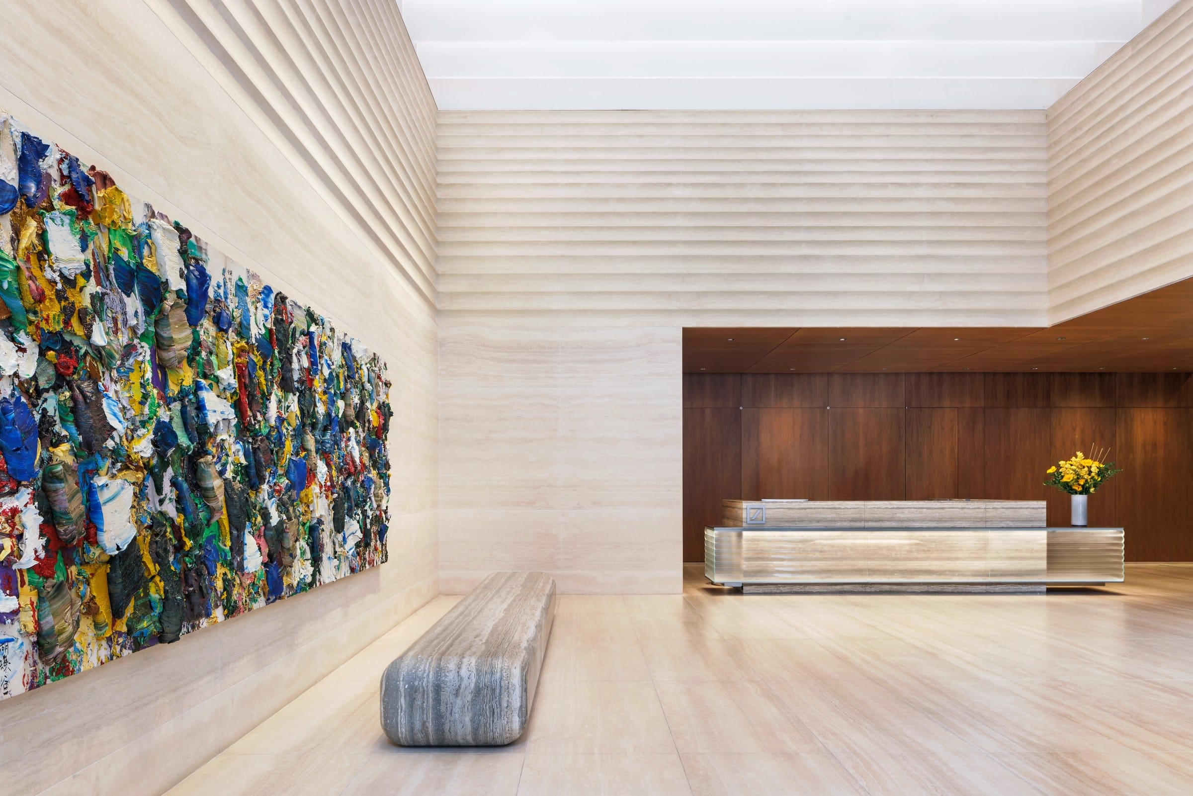 Stone lobby with a long multicolored impasto painting above a stone bench and a reception desk beyond