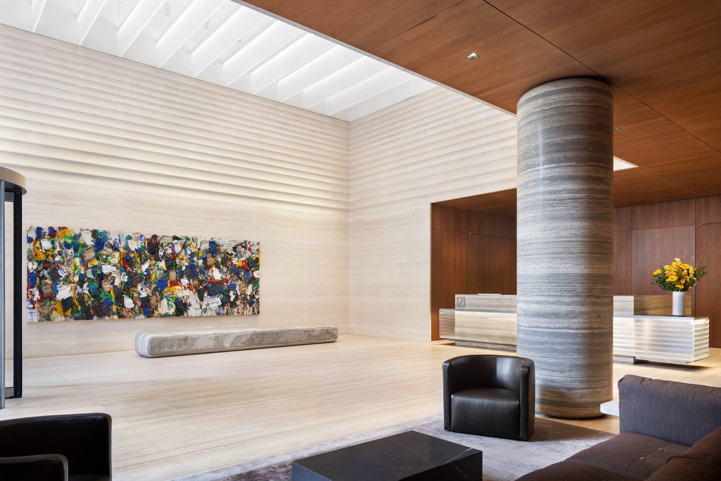 Lobby seating behind a striped stone column, looking toward a long multicolored painting and reception desk