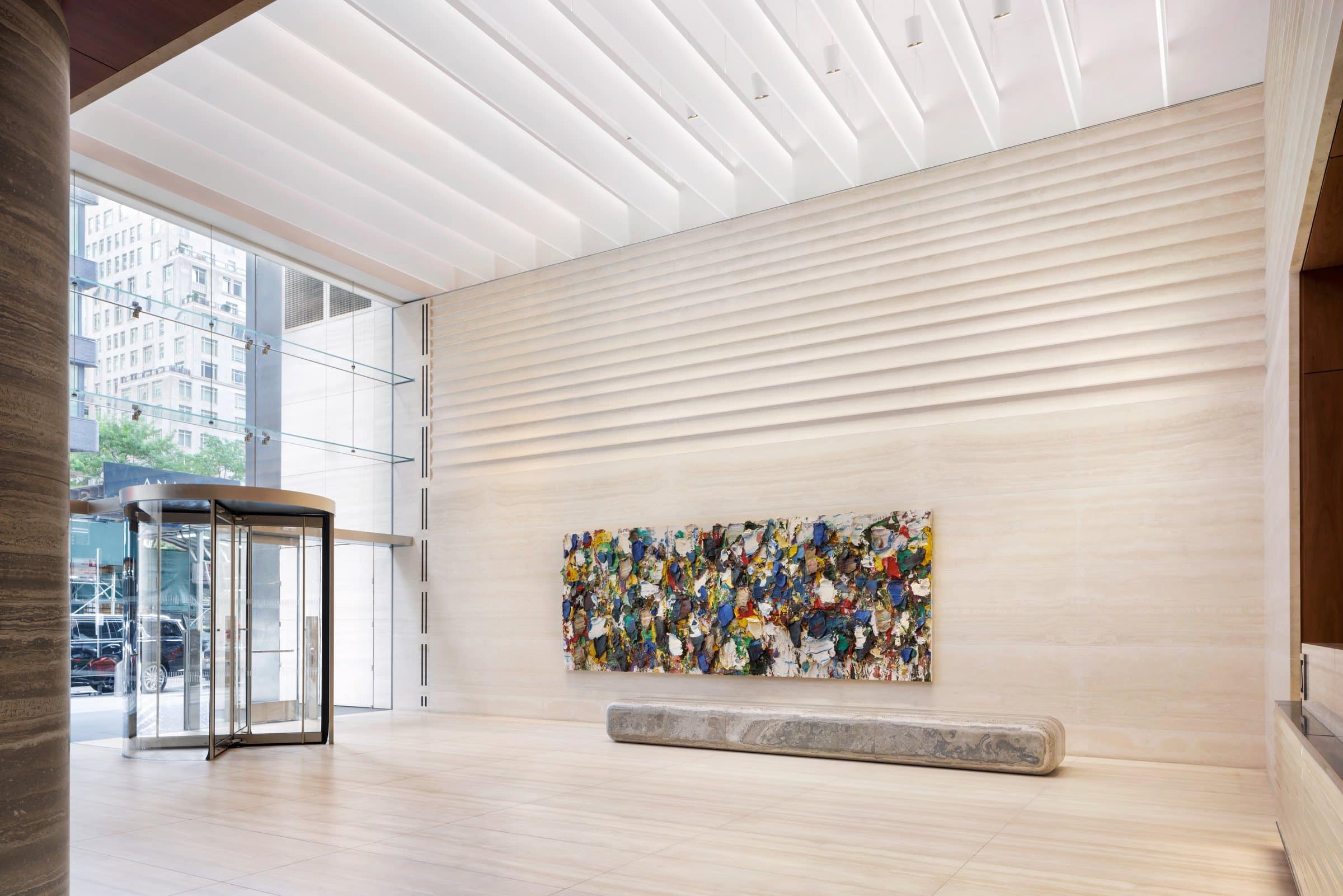 Double-height lobby with a revolving glass door and a multicolored impasto painting on a ridged stone wall