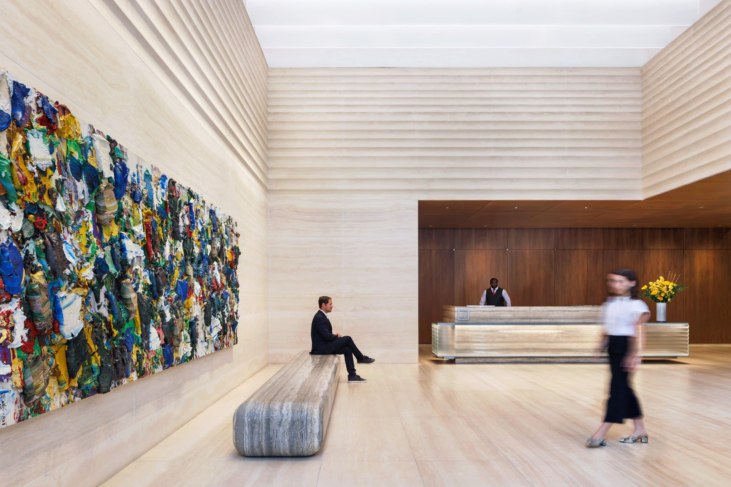 Visitors sitting and walking beneath a long colorful impasto painting, with the reception desk beyond