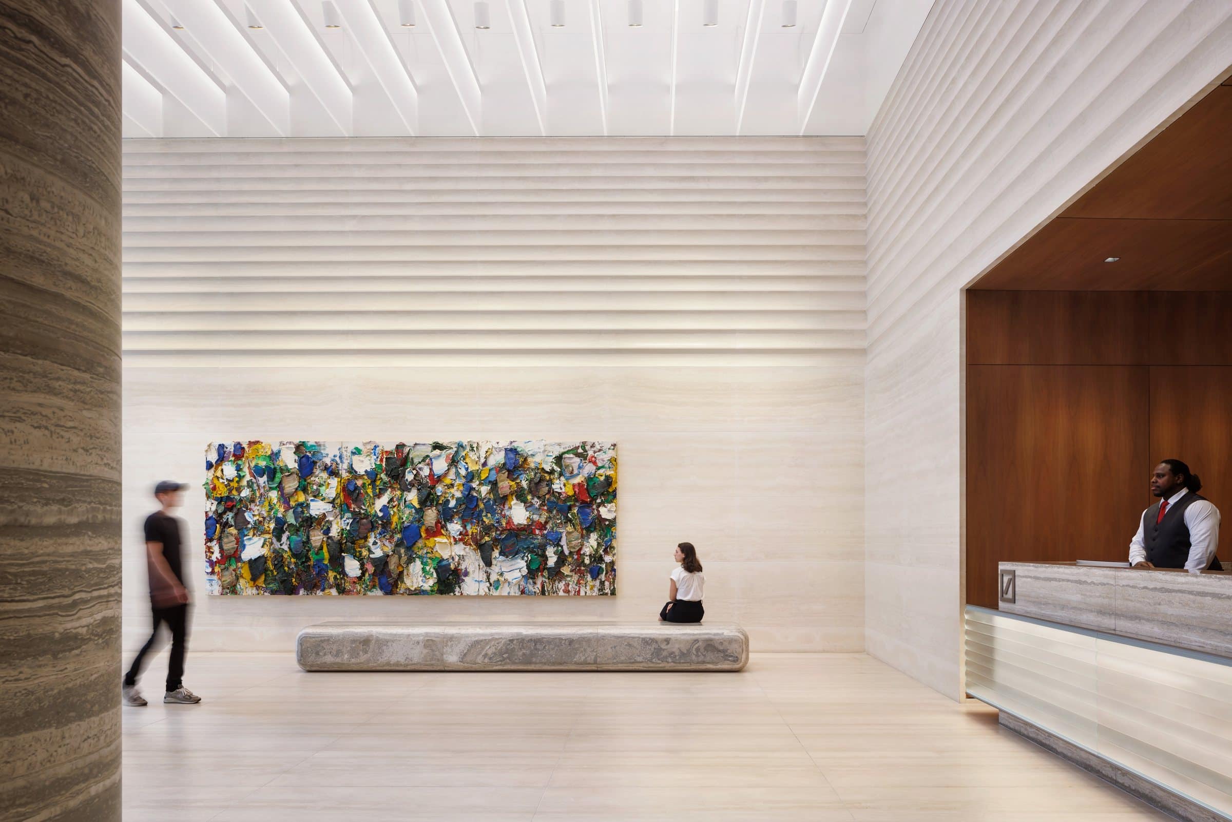 A seated visitor and a walking figure give scale to the multicolored painting across the stone lobby