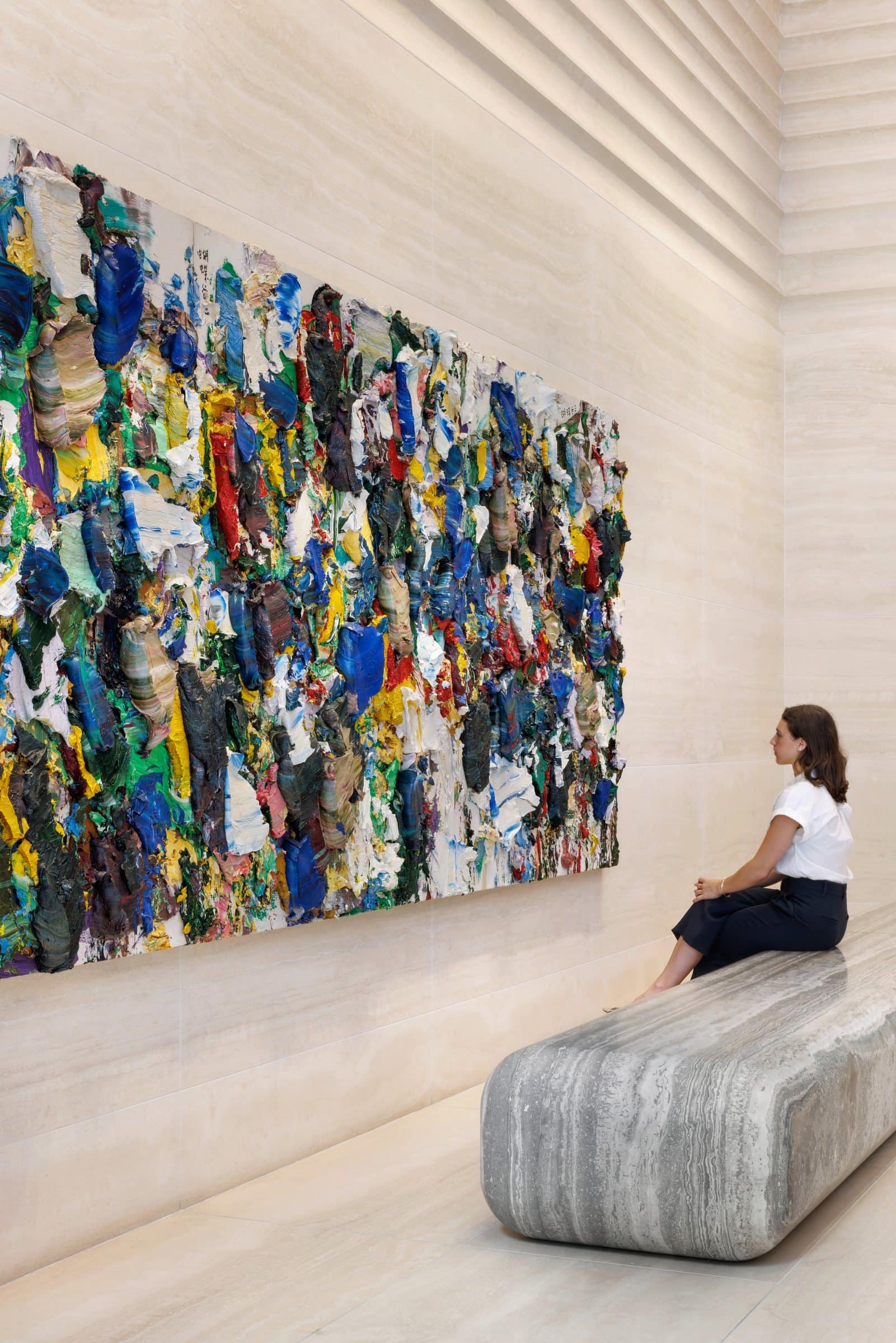 A visitor seated on the stone bench beneath an angled close view of the heavily textured painting