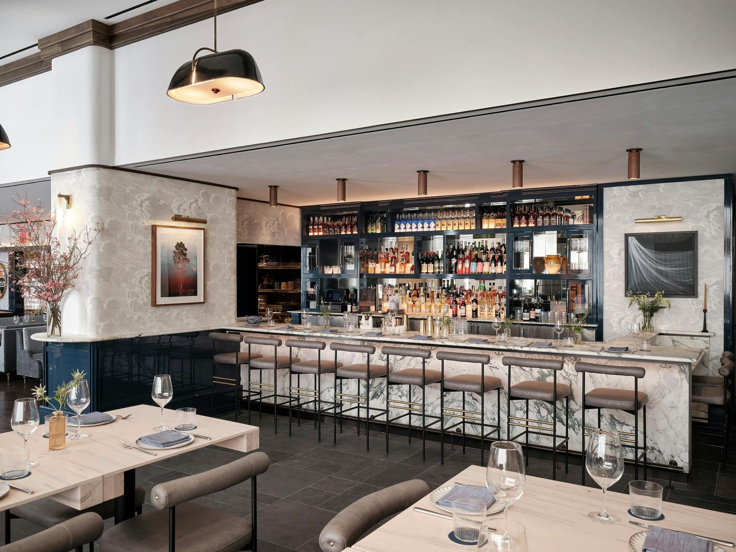Greywind bar with a marble counter and gray stools, flanked by a photograph of a tree and a dark work of flowing white lines