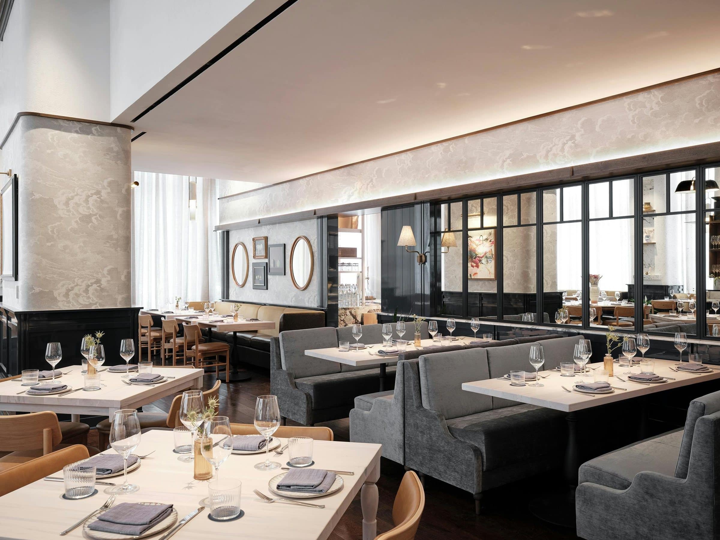 Greywind dining room with gray booths, a mirrored partition and small framed paintings and oval mirrors on the far wall