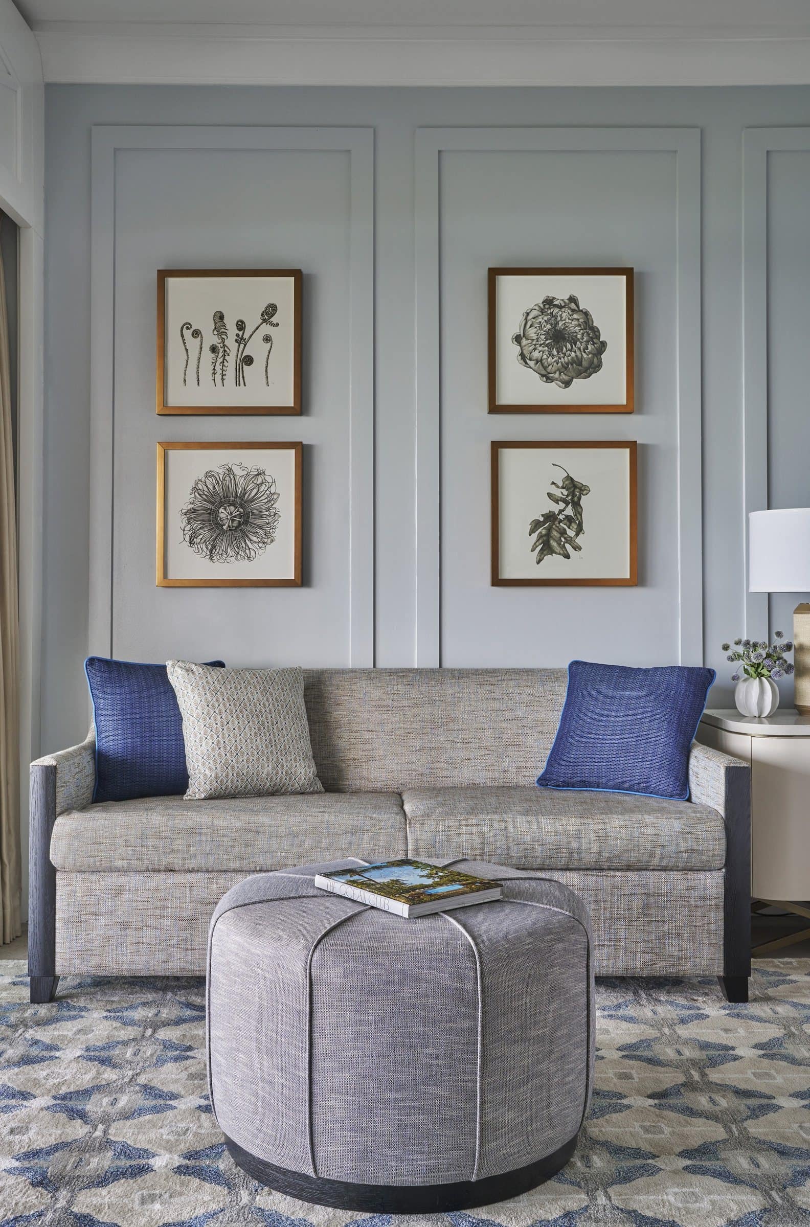 Suite bedroom seating area with four black-and-white botanical works in gold frames above a gray sofa