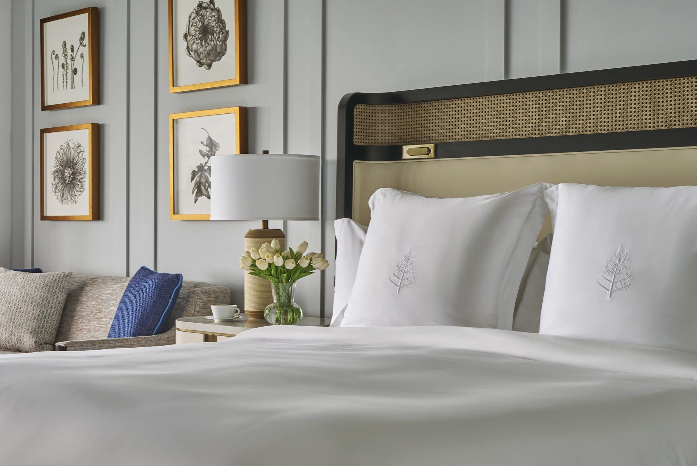 Close view of the king bed and bedside lamp, with four framed botanical works on the paneled wall to the left