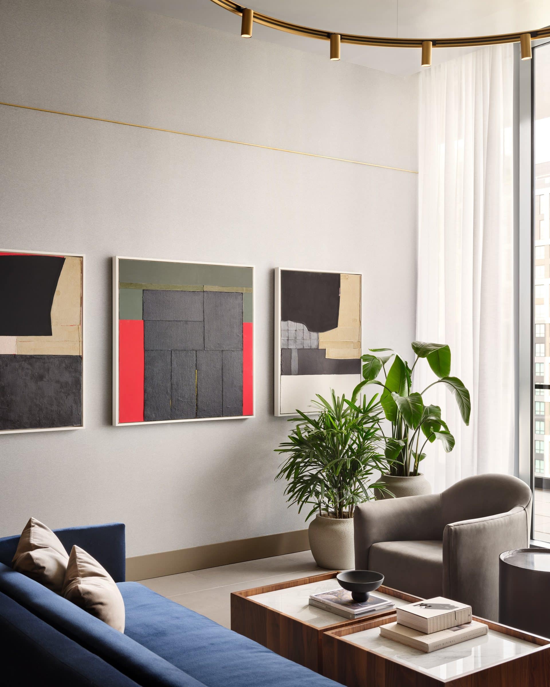 Lounge with a blue sofa, gray armchair and three framed geometric works in black, cream, gray, red and green