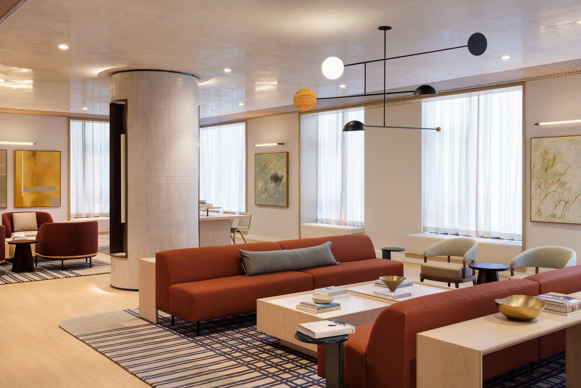 Bright lounge with rust-colored sofas, a yellow geometric painting and two pale gestural paintings between the windows