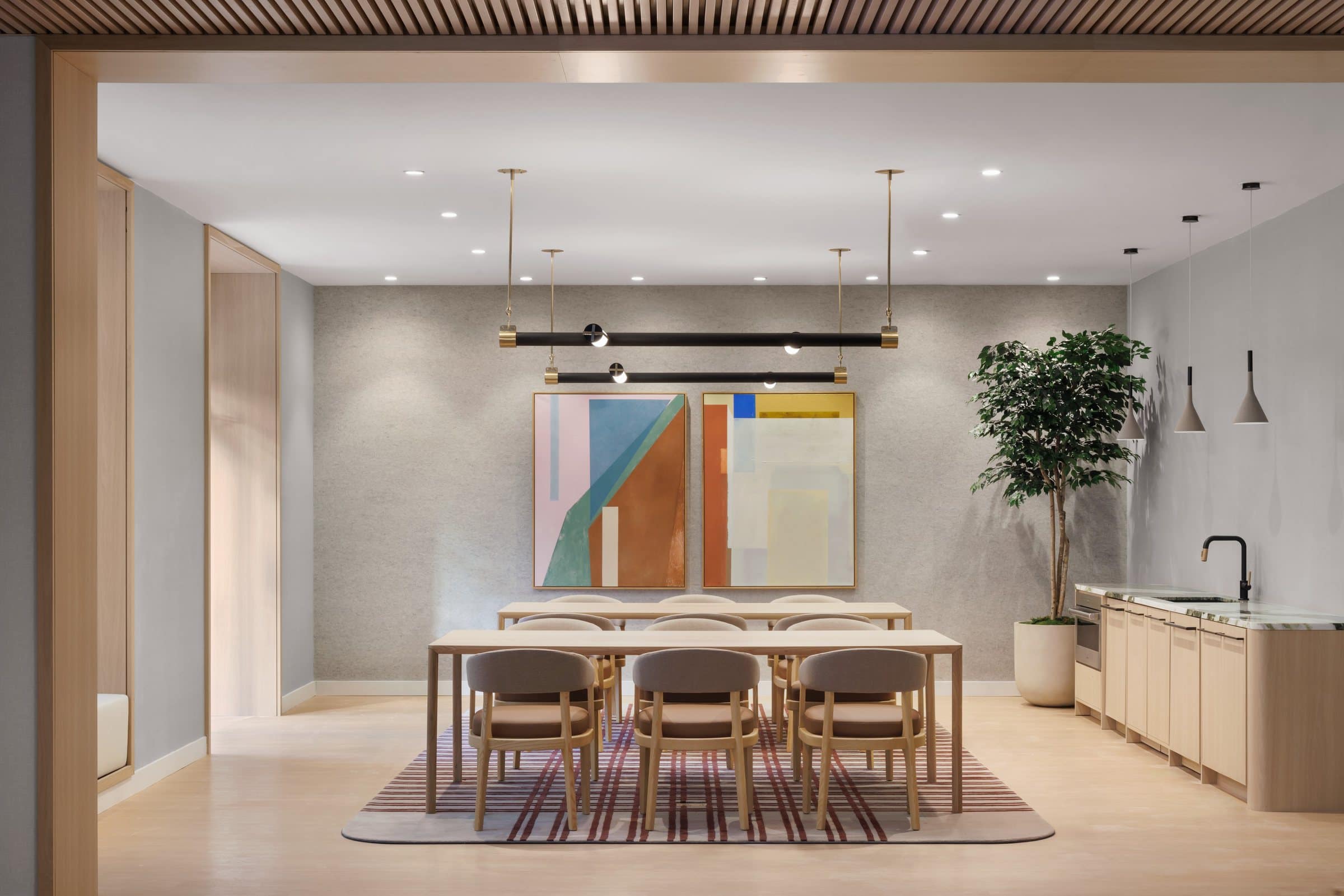 Dining room with a long pale table and two geometric paintings in ochre, green, pink, blue and cream