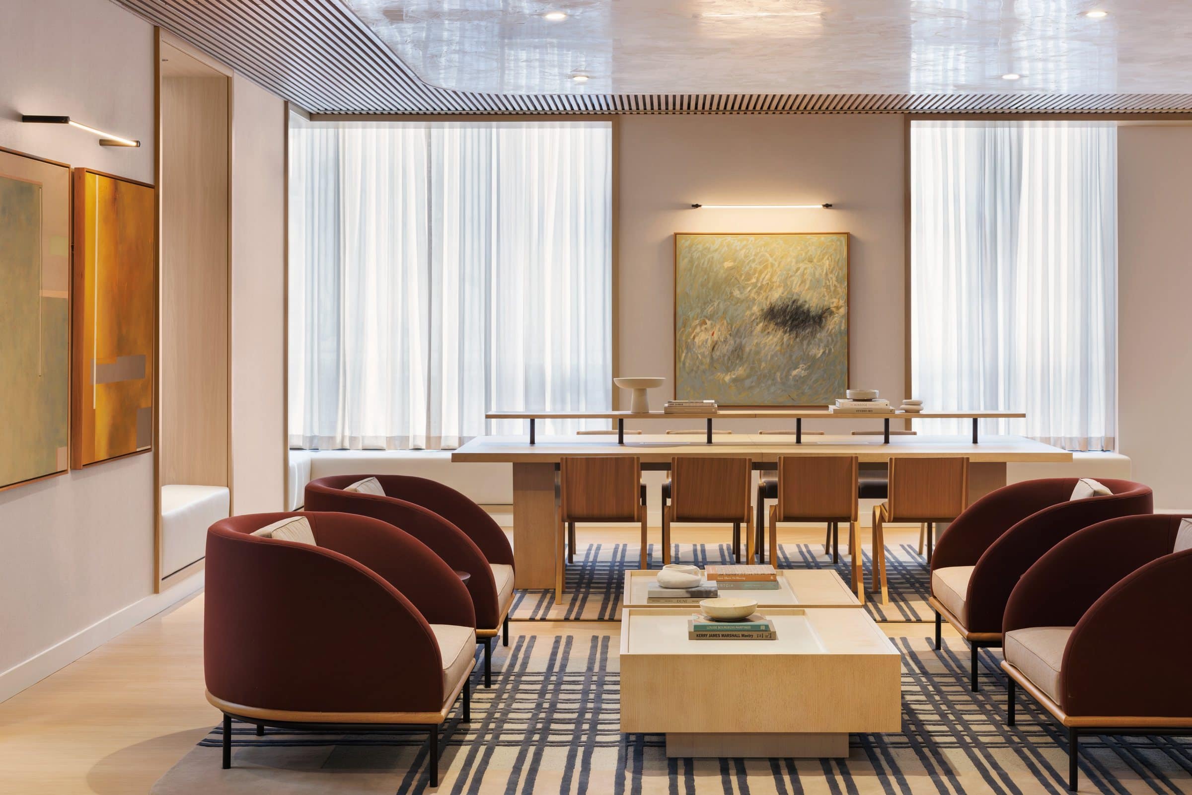 Rust-colored lounge chairs and a pale table beneath a green-gray gestural painting, with geometric canvases at left