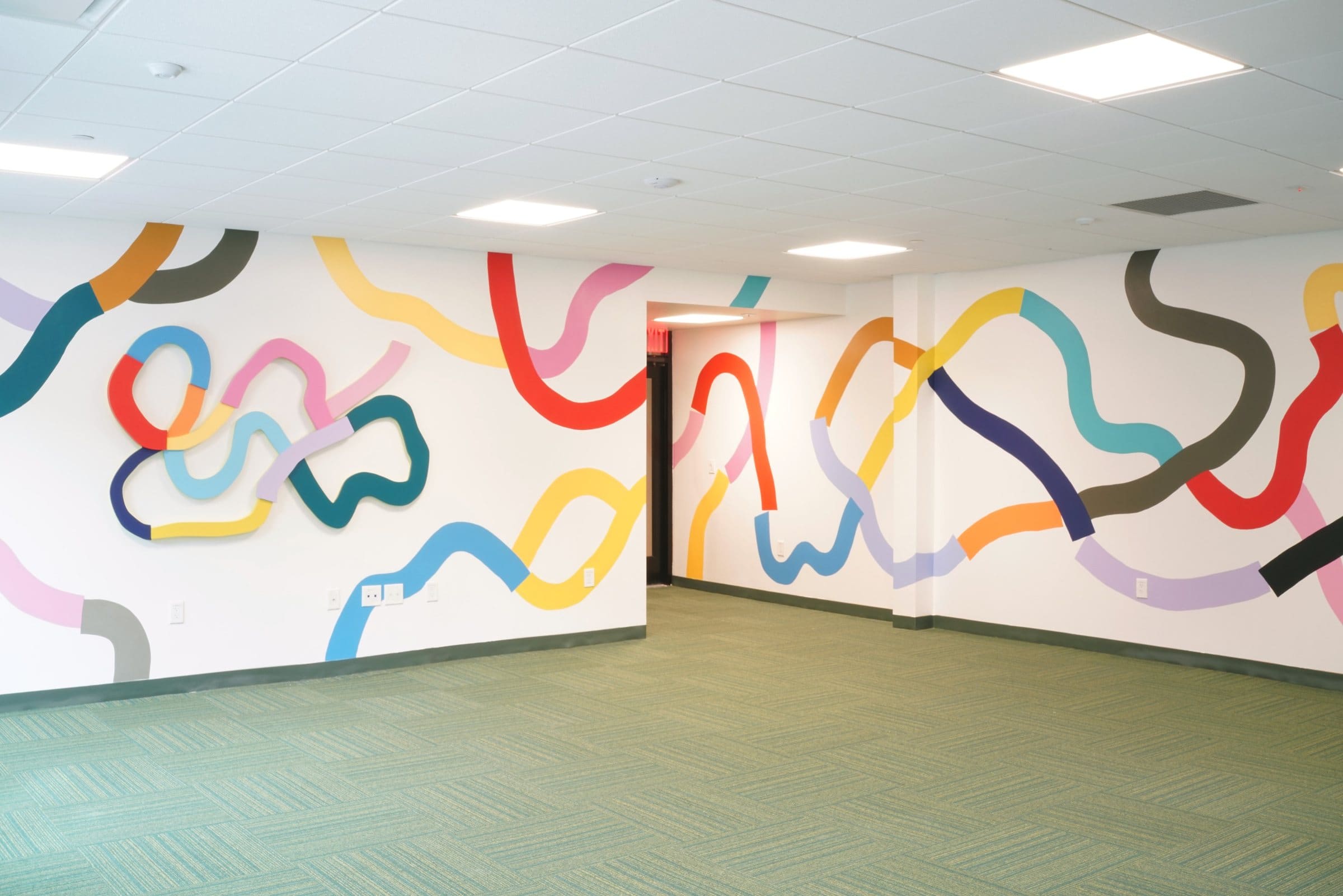 Colorful looping mural lines and a dimensional wall sculpture fill a children’s room at Harriet Tubman Supportive Housing Building.