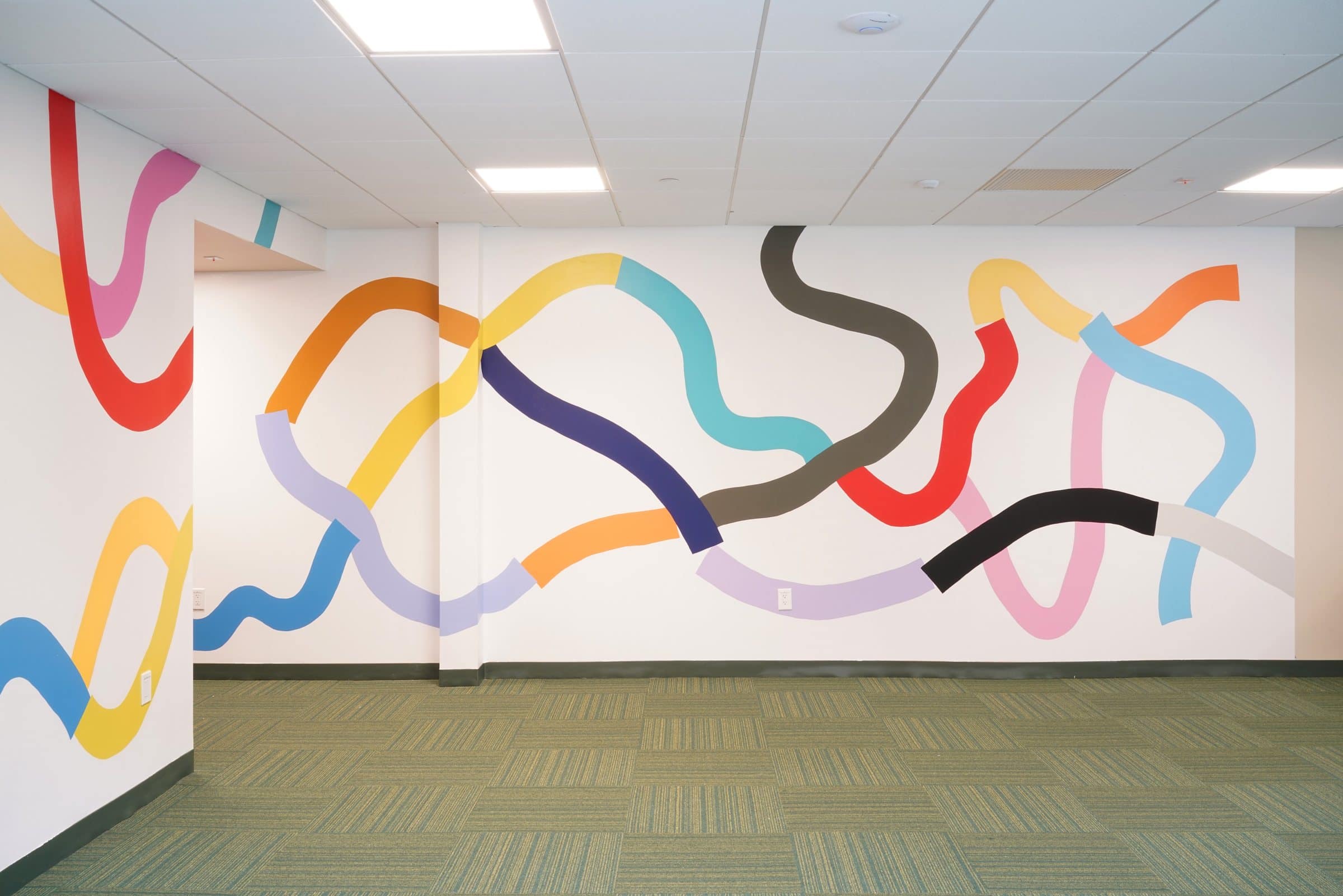 A broad wall carries a mural of interwoven colorful lines at Harriet Tubman Supportive Housing Building.
