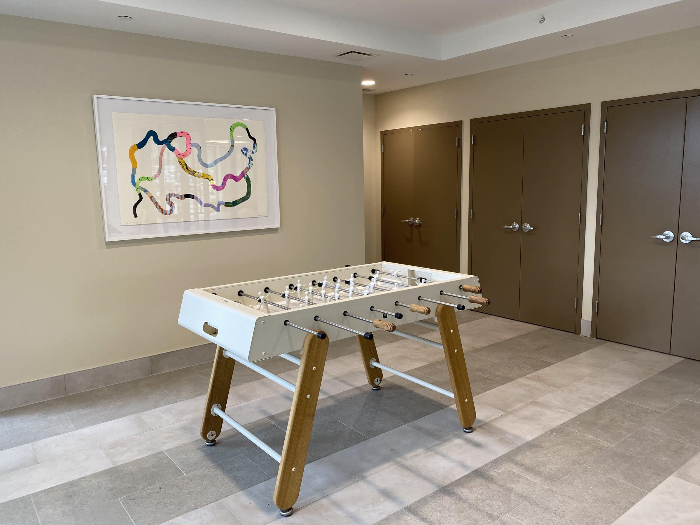 A framed looping paper collage hangs above a foosball table at Harriet Tubman Supportive Housing Building.