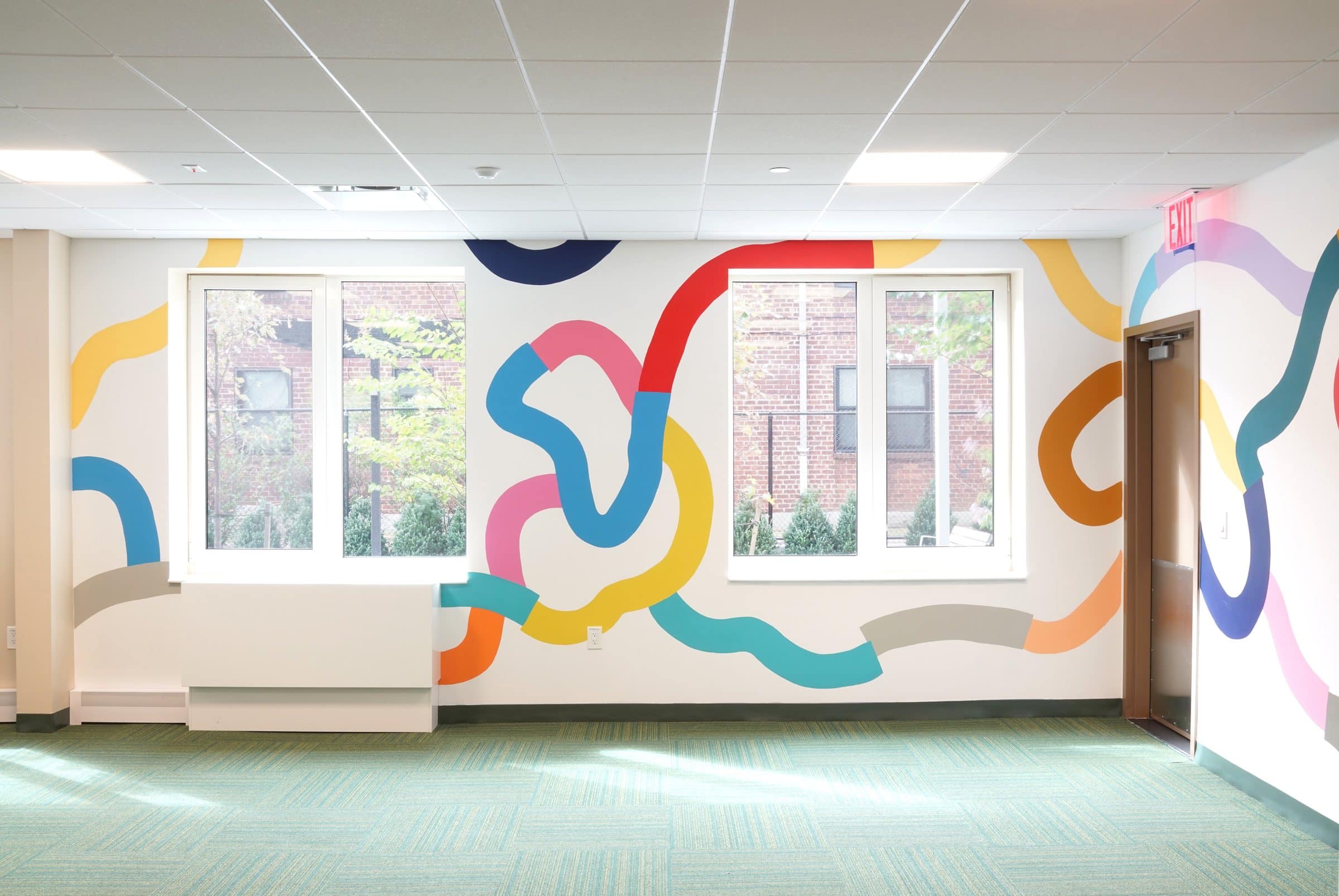 Colorful mural lines flow around two windows at Harriet Tubman Supportive Housing Building.