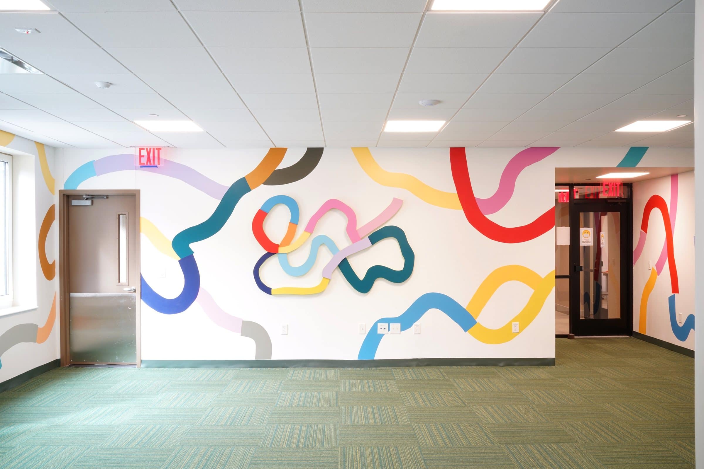 A wall sculpture of colorful looping forms sits within a painted mural at Harriet Tubman Supportive Housing Building.