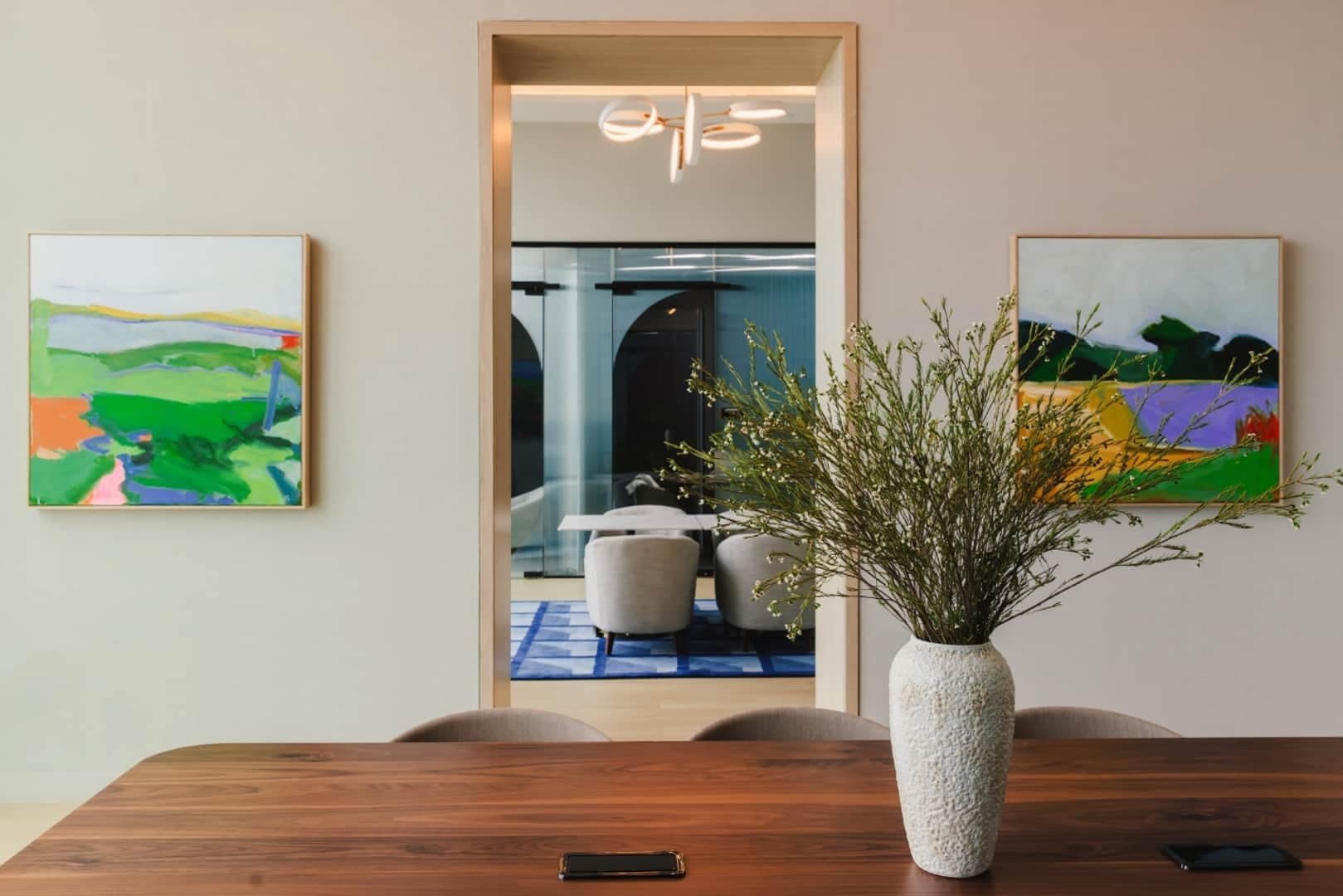 Two colorful landscape paintings flank a doorway beside a shared work table at Linea.