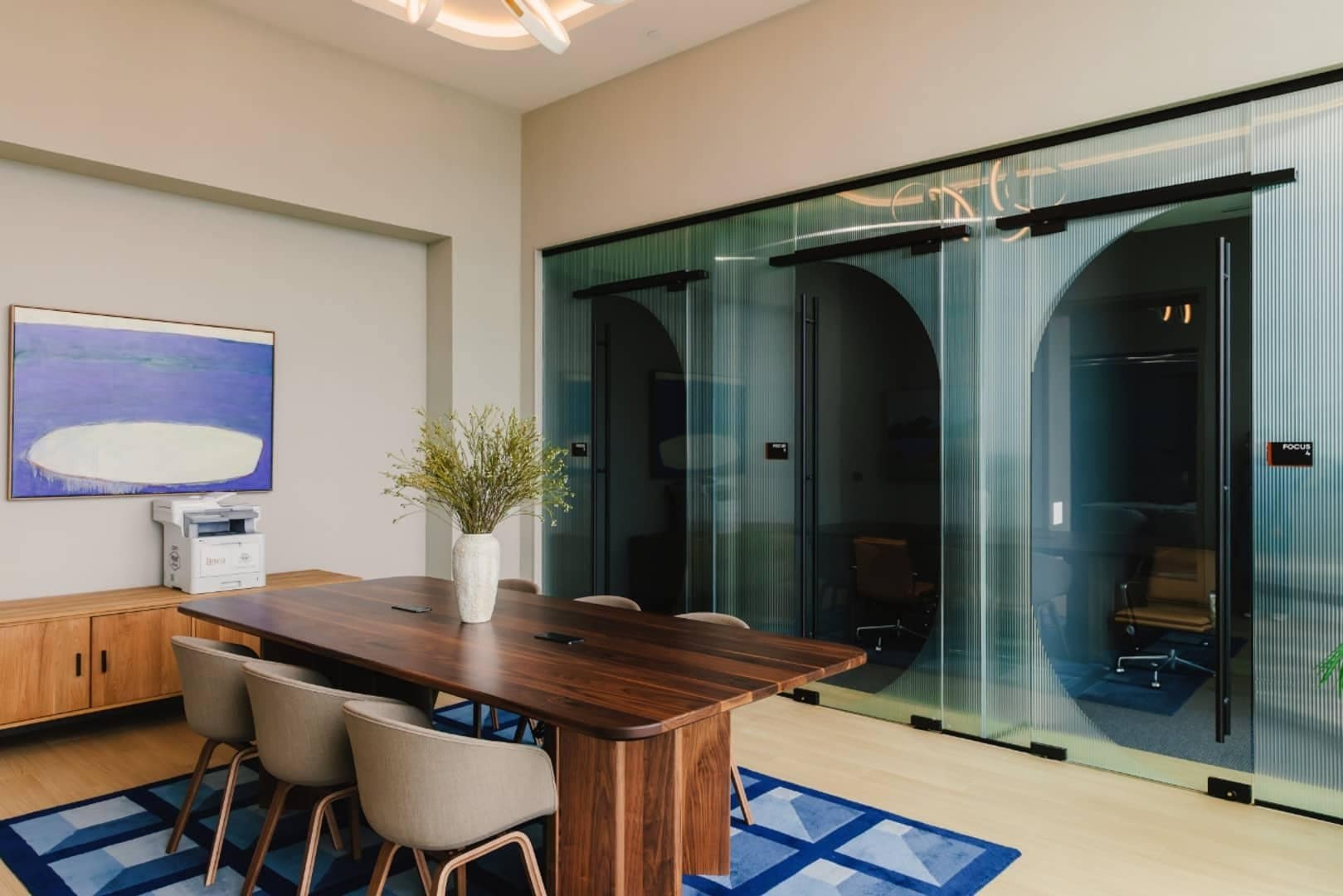 A blue painting with a white oval above a cabinet beside a shared work table at Linea.