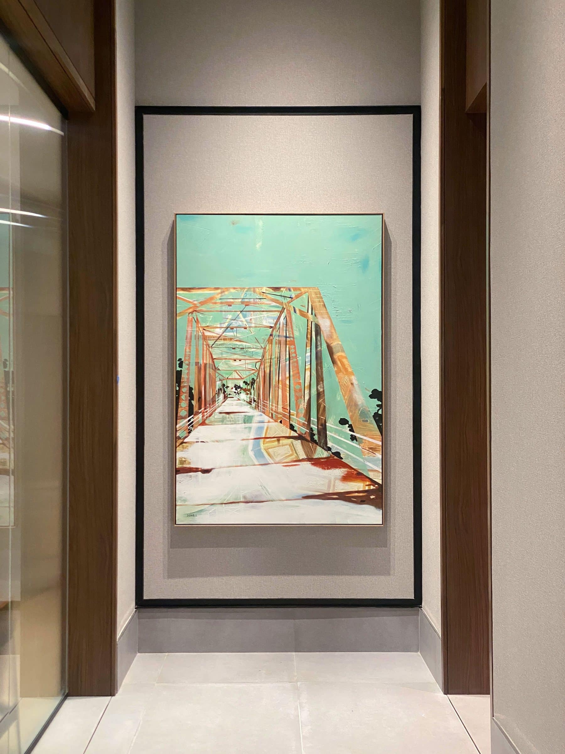 A painting of a truss bridge against a turquoise sky hangs in a Linea corridor.