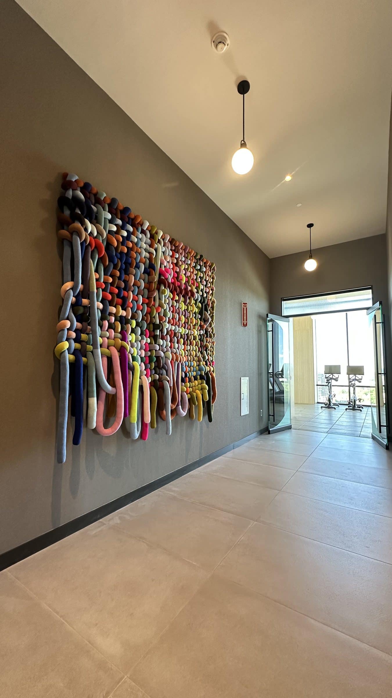 A large multicolored knotted textile work hangs along a Linea amenity corridor.
