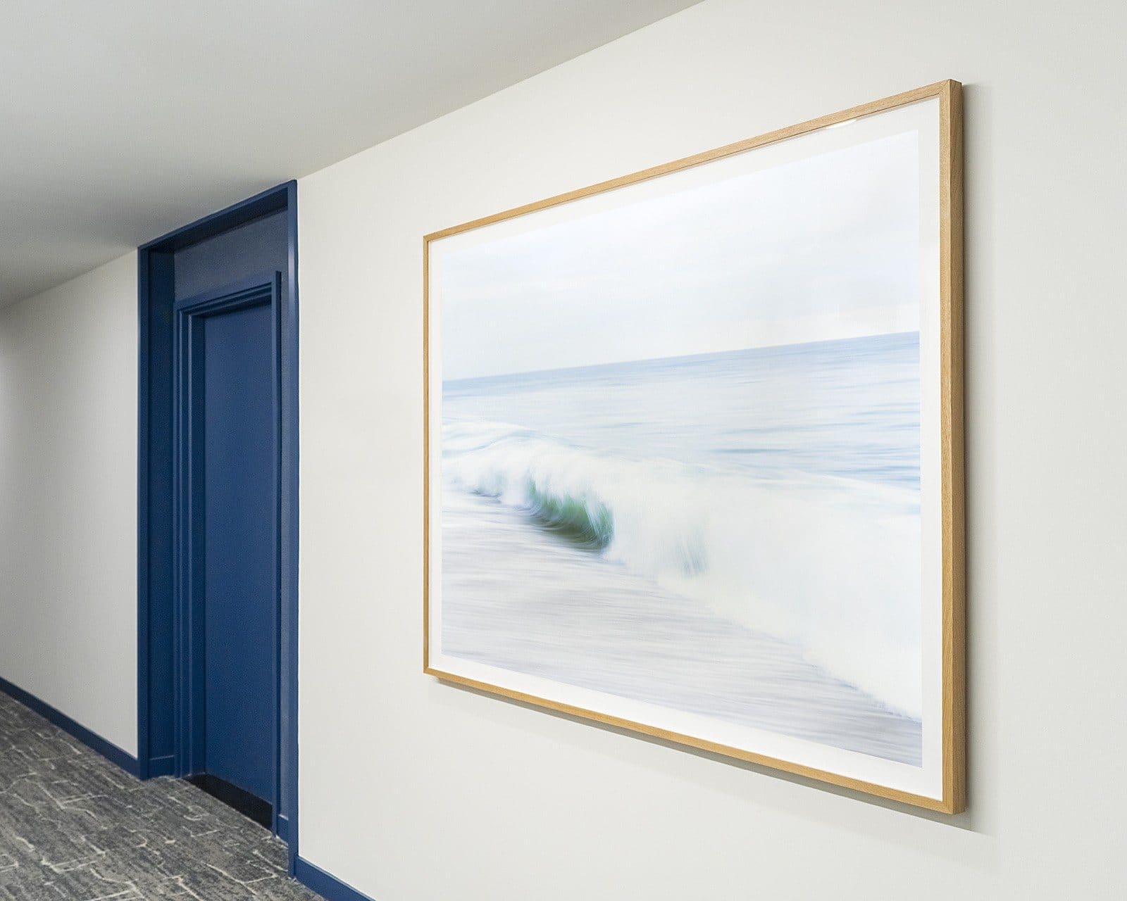 A framed photograph of a breaking wave hangs beside a blue door at SURFHOUSE Asbury Park.