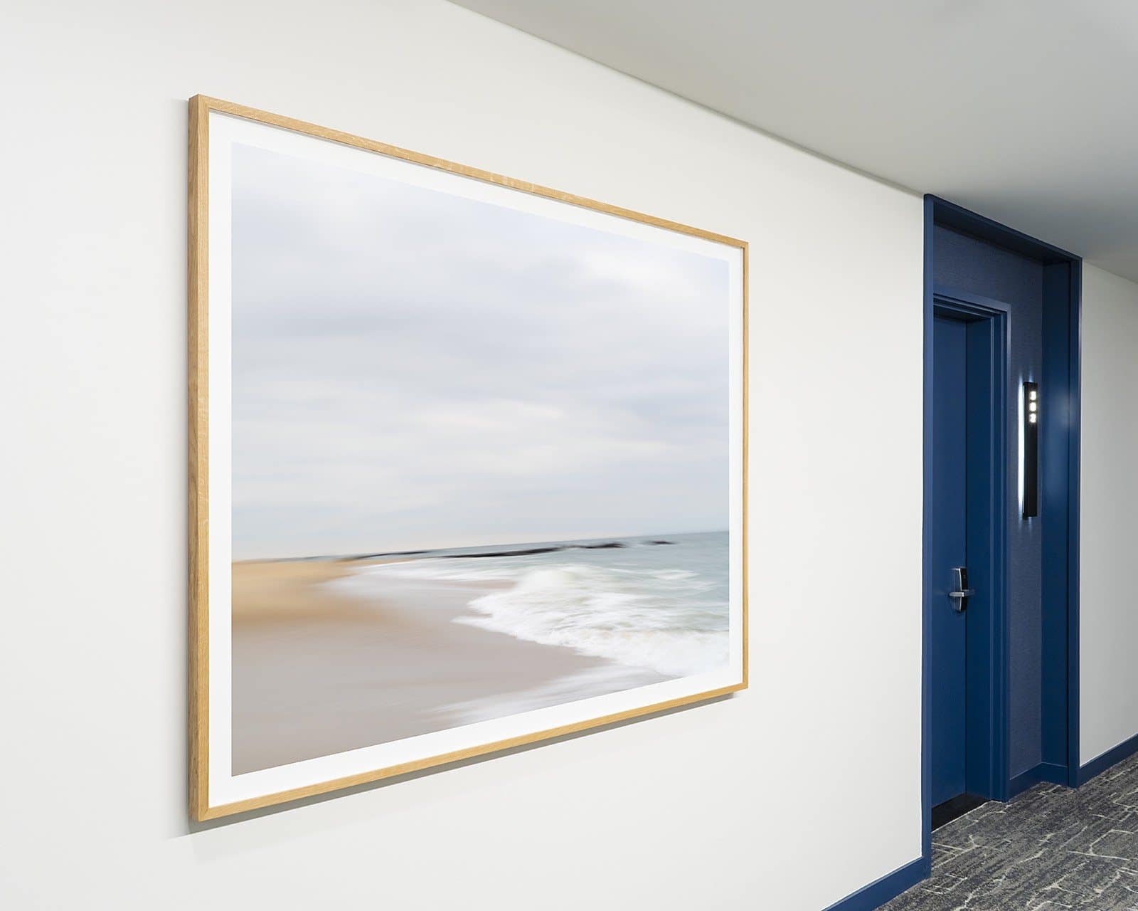 A framed photograph of waves along a beach hangs beside a blue door at SURFHOUSE Asbury Park.