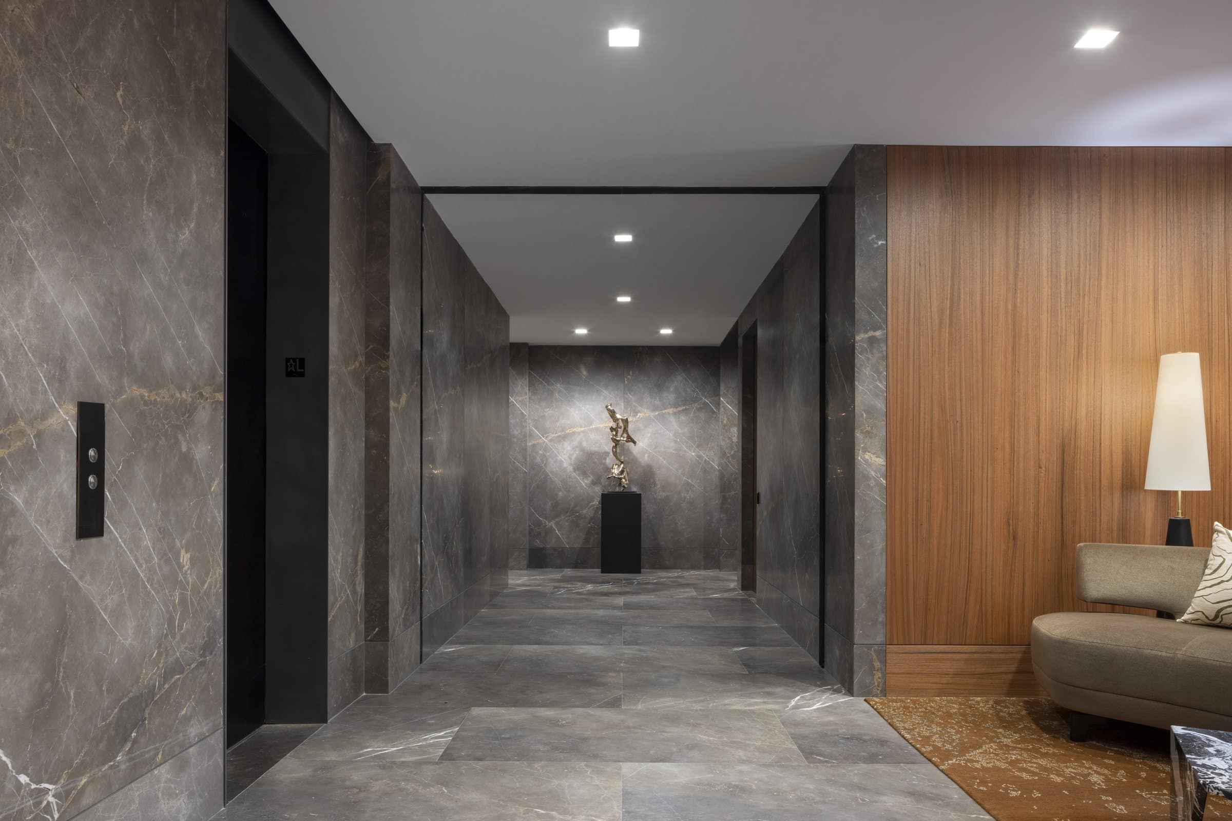 View down a stone corridor to a bronze sculpture on a black plinth, with a lounge alcove at right