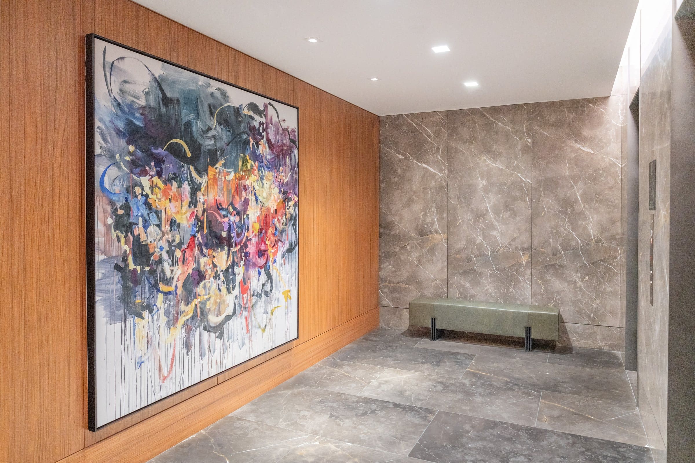 Large navy, violet, yellow and orange gestural painting on wood paneling beside a green bench in a stone vestibule