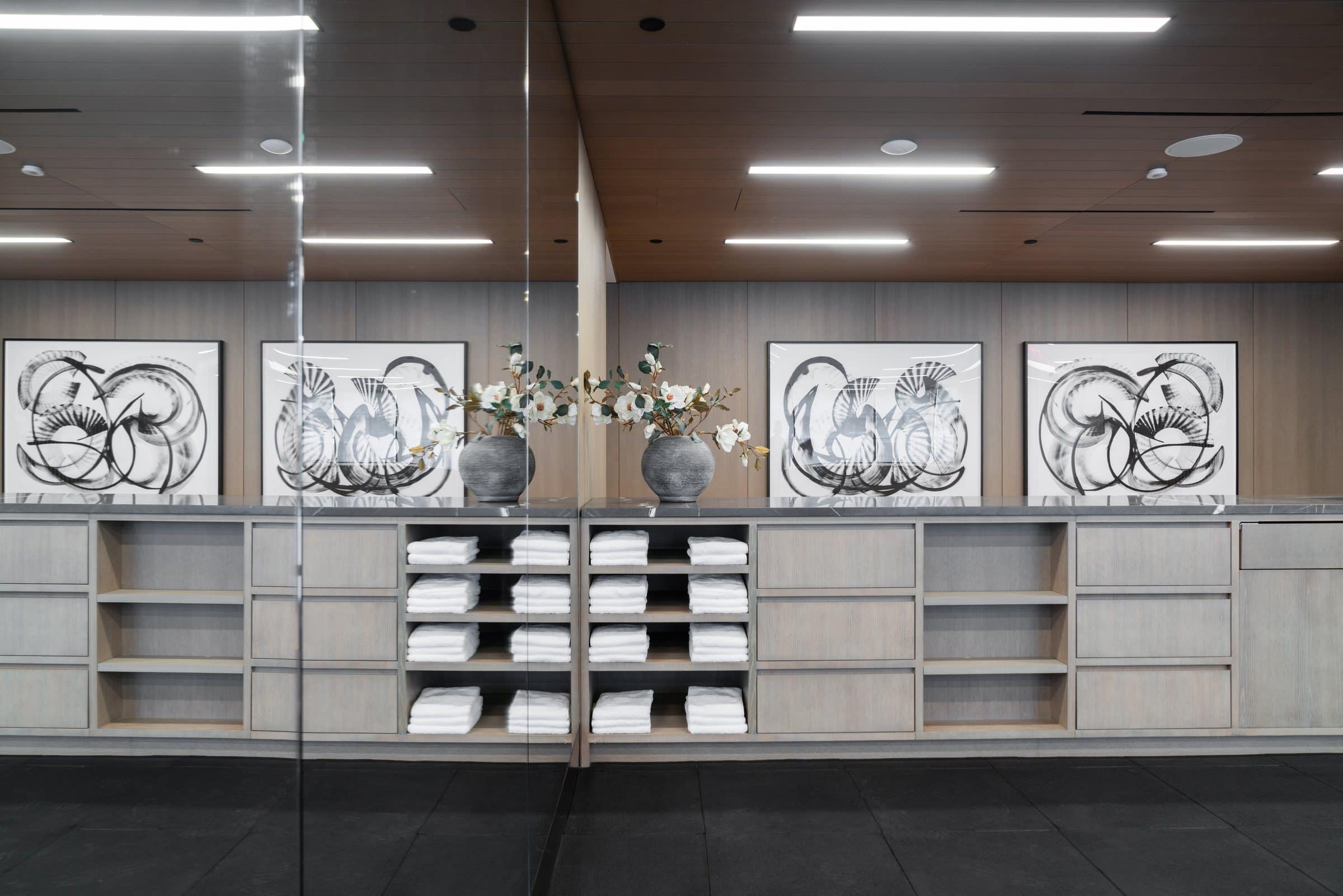 Black gestural works on white above towel shelves in a mirrored fitness room; the mirror repeats the pair