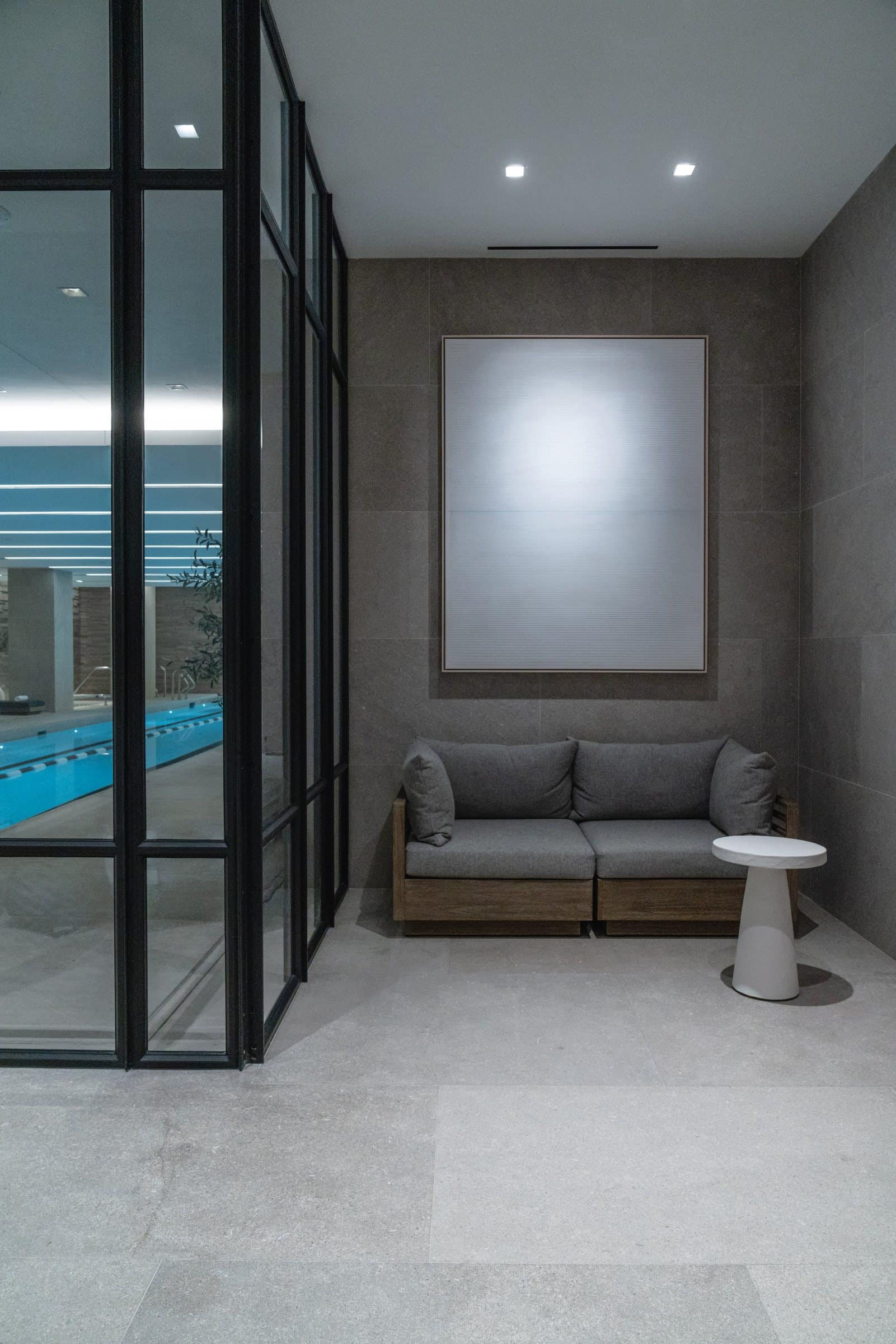 Pale atmospheric framed work above a gray bench beside glass doors to the indoor pool