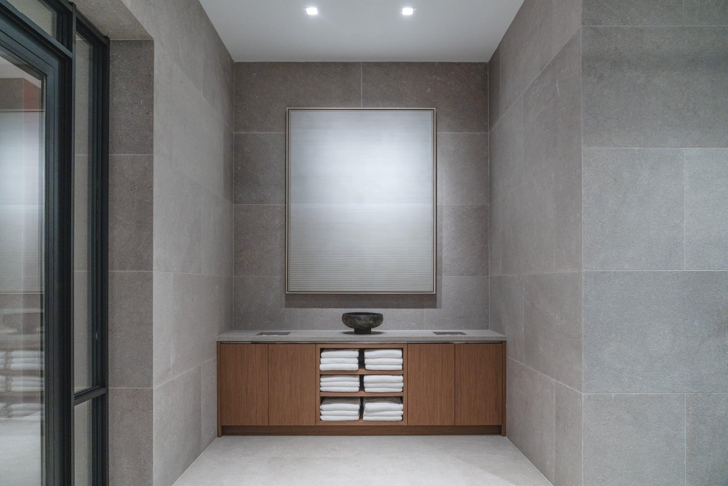 Pale atmospheric framed work above a wood cabinet with towels in a stone-walled alcove