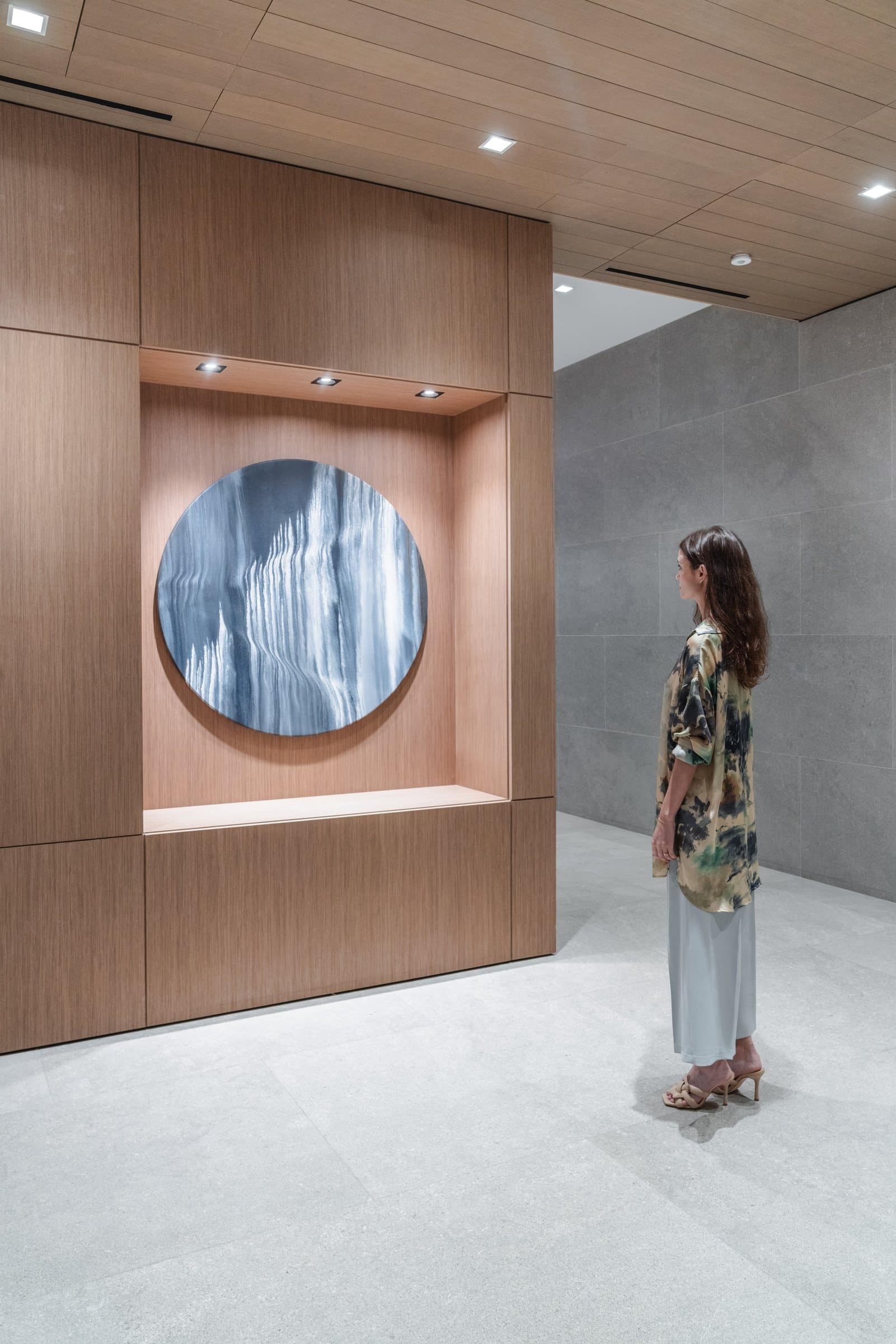 A visitor stands beside the circular blue-and-white abstract work in a wood-paneled niche