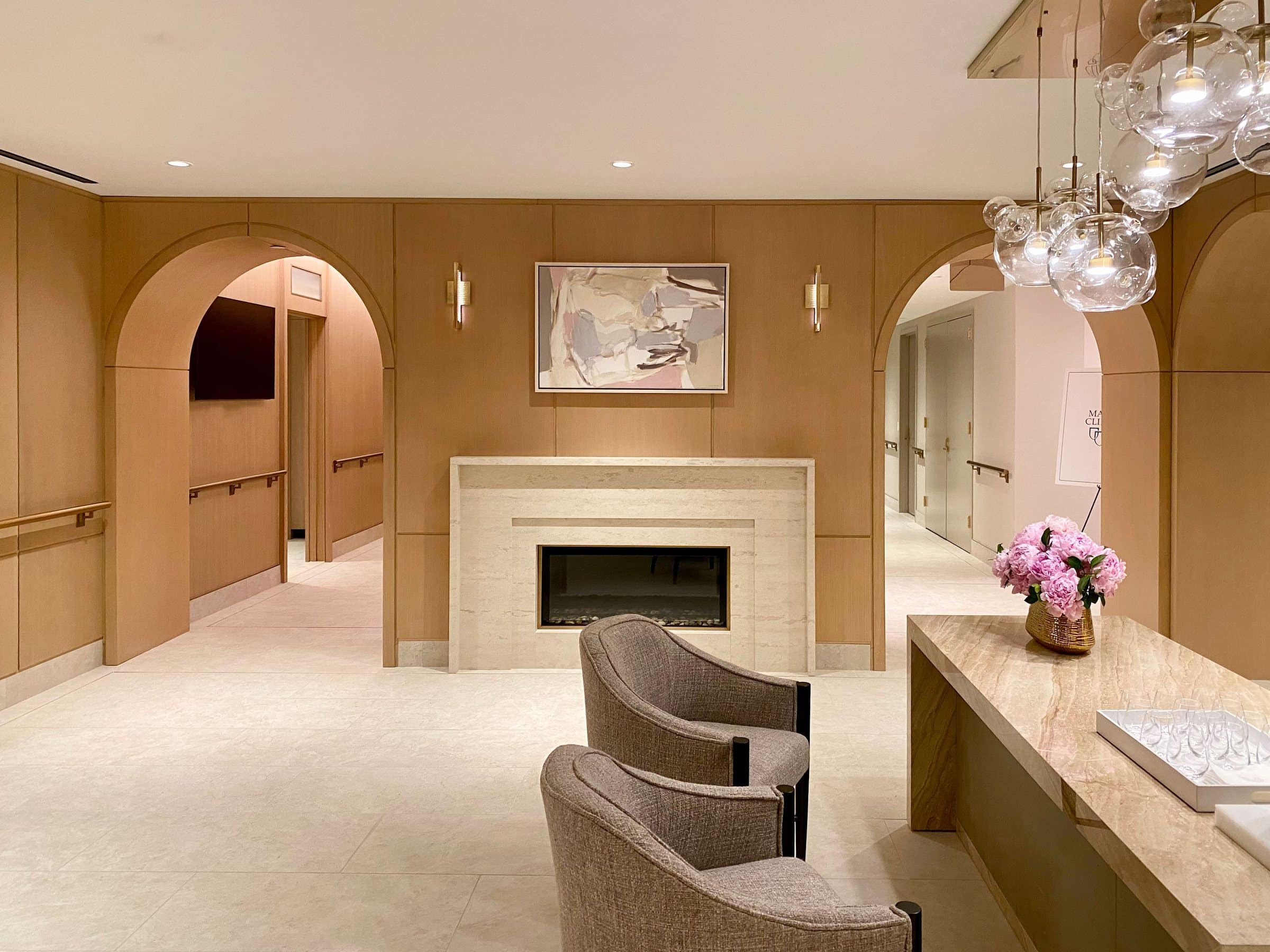 Warm wood-paneled lounge with arched doorways and a pale abstract work above a stone fireplace