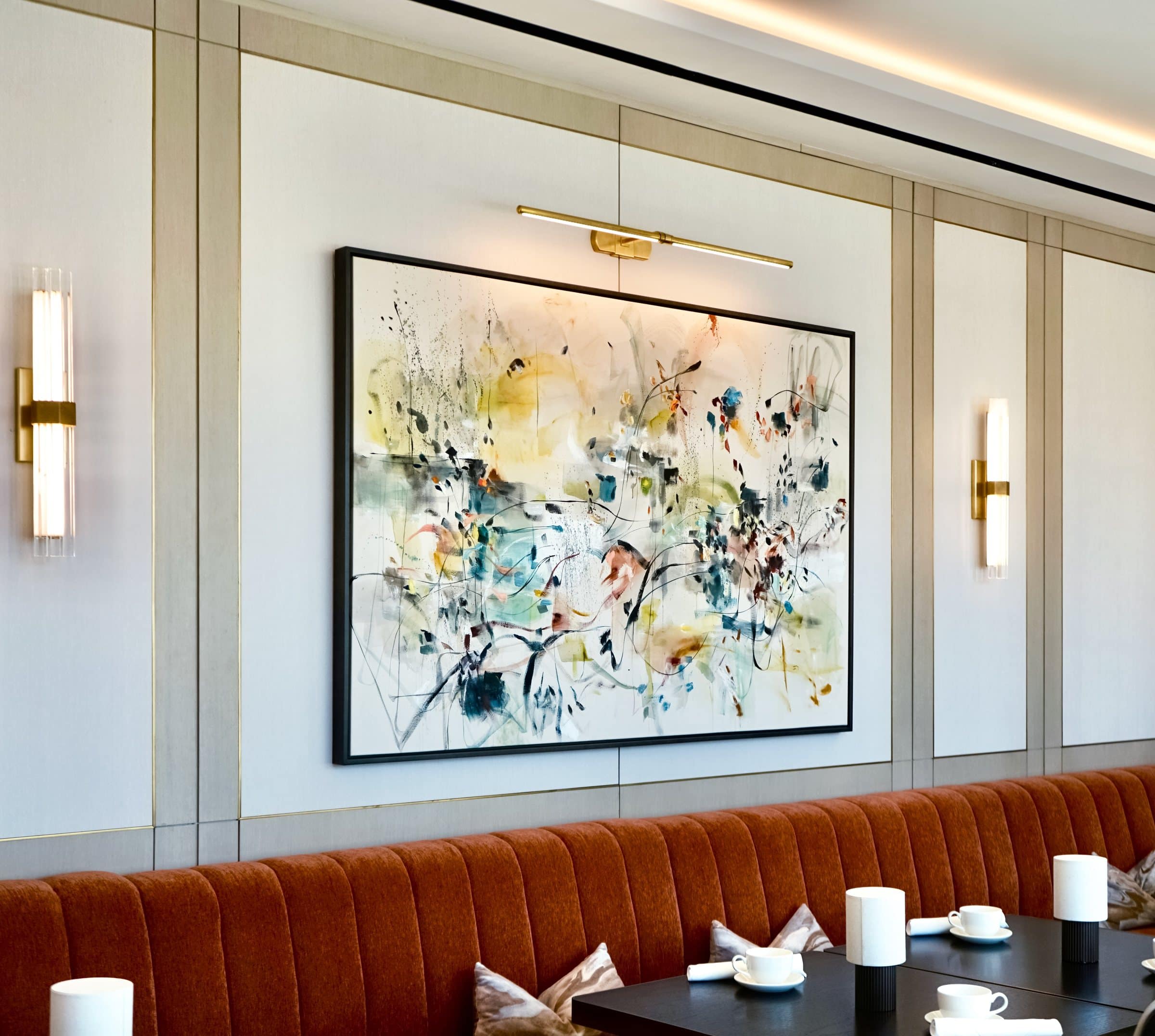 Angled close view of the light yellow, blue and black gestural painting above the orange banquette