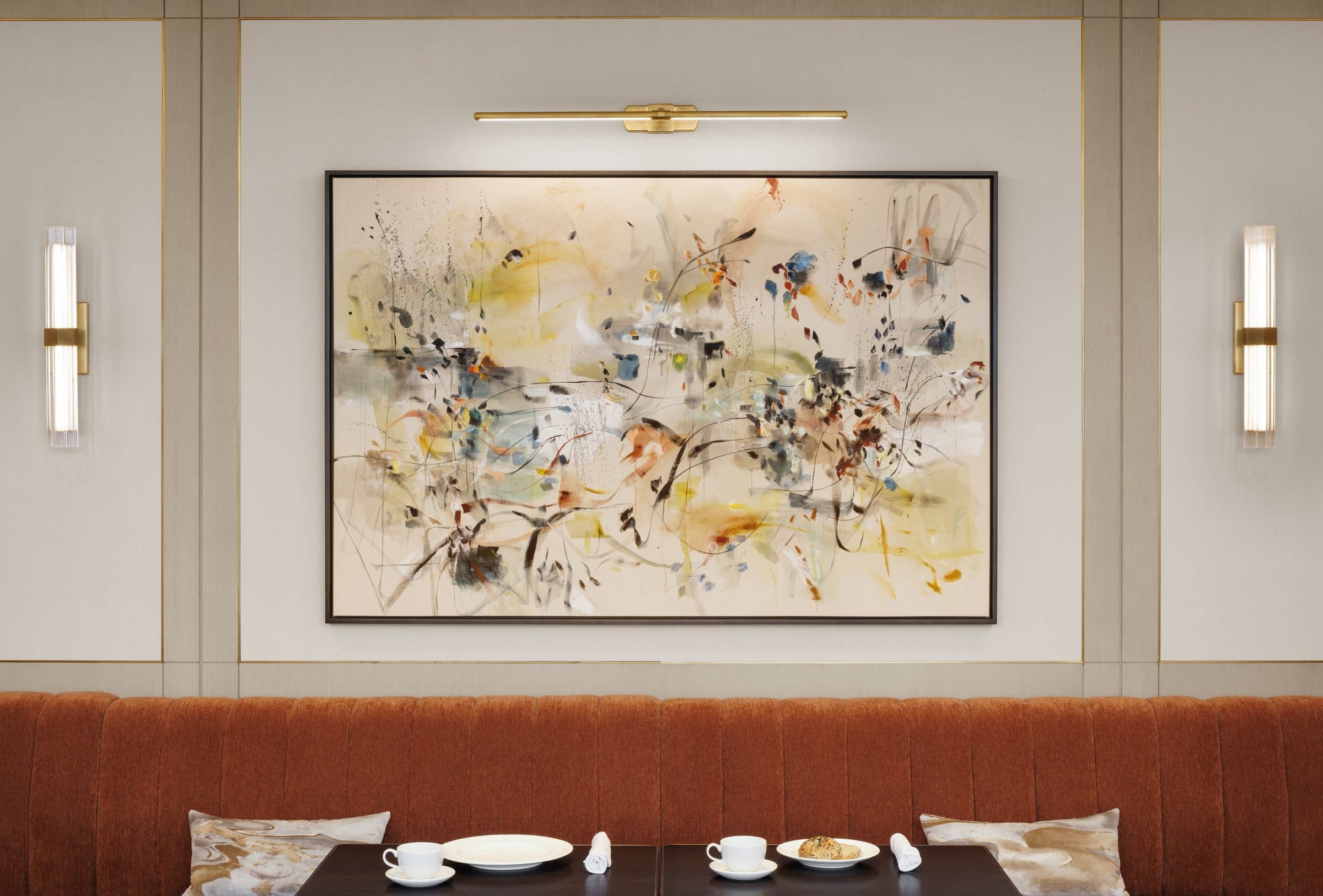 Light gestural abstract painting with yellow, blue and black accents above an orange dining banquette