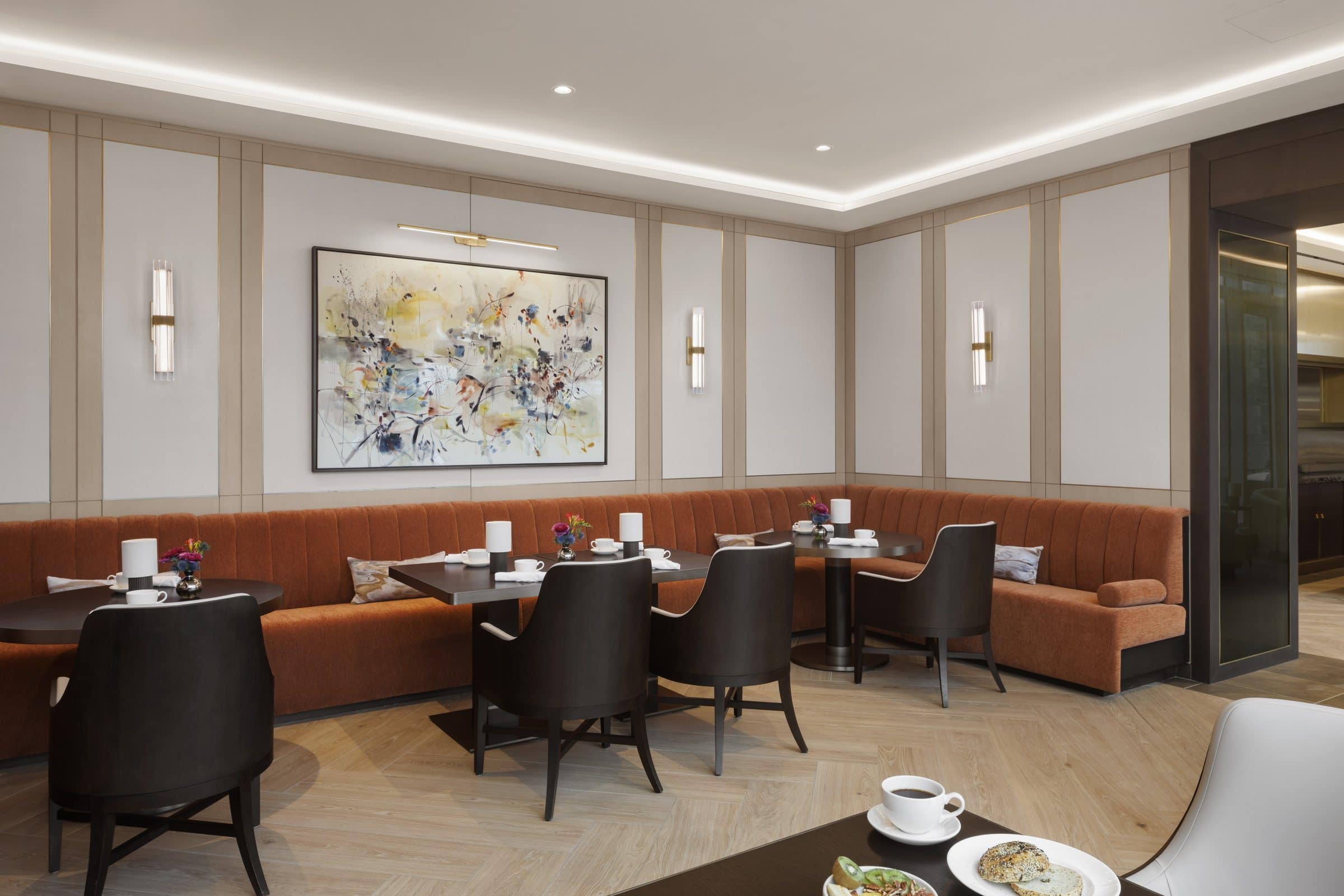 Dining tables and an orange corner banquette beneath a light gestural abstract painting