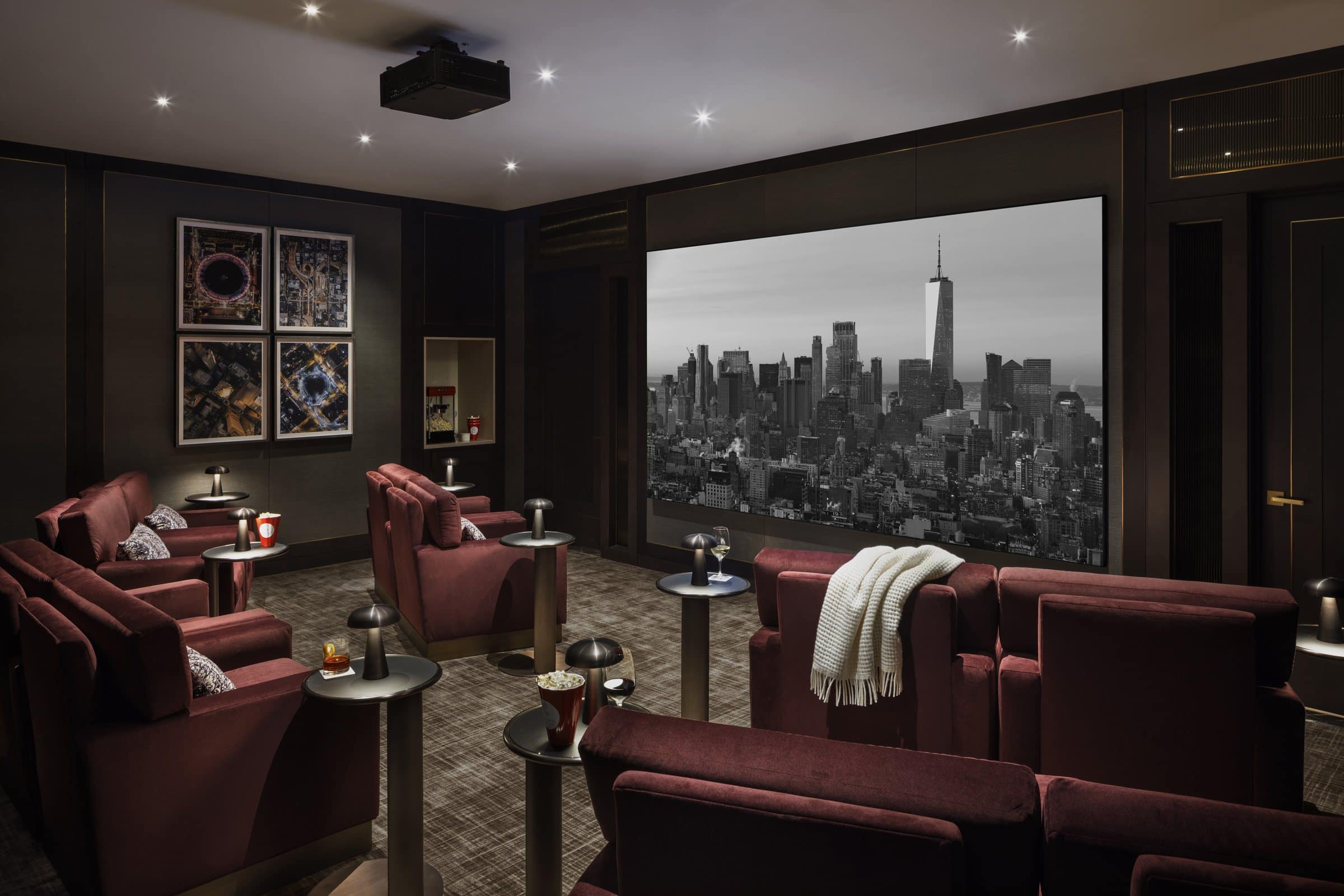 Dark screening room with burgundy chairs and four framed nighttime aerial photographs beside the screen