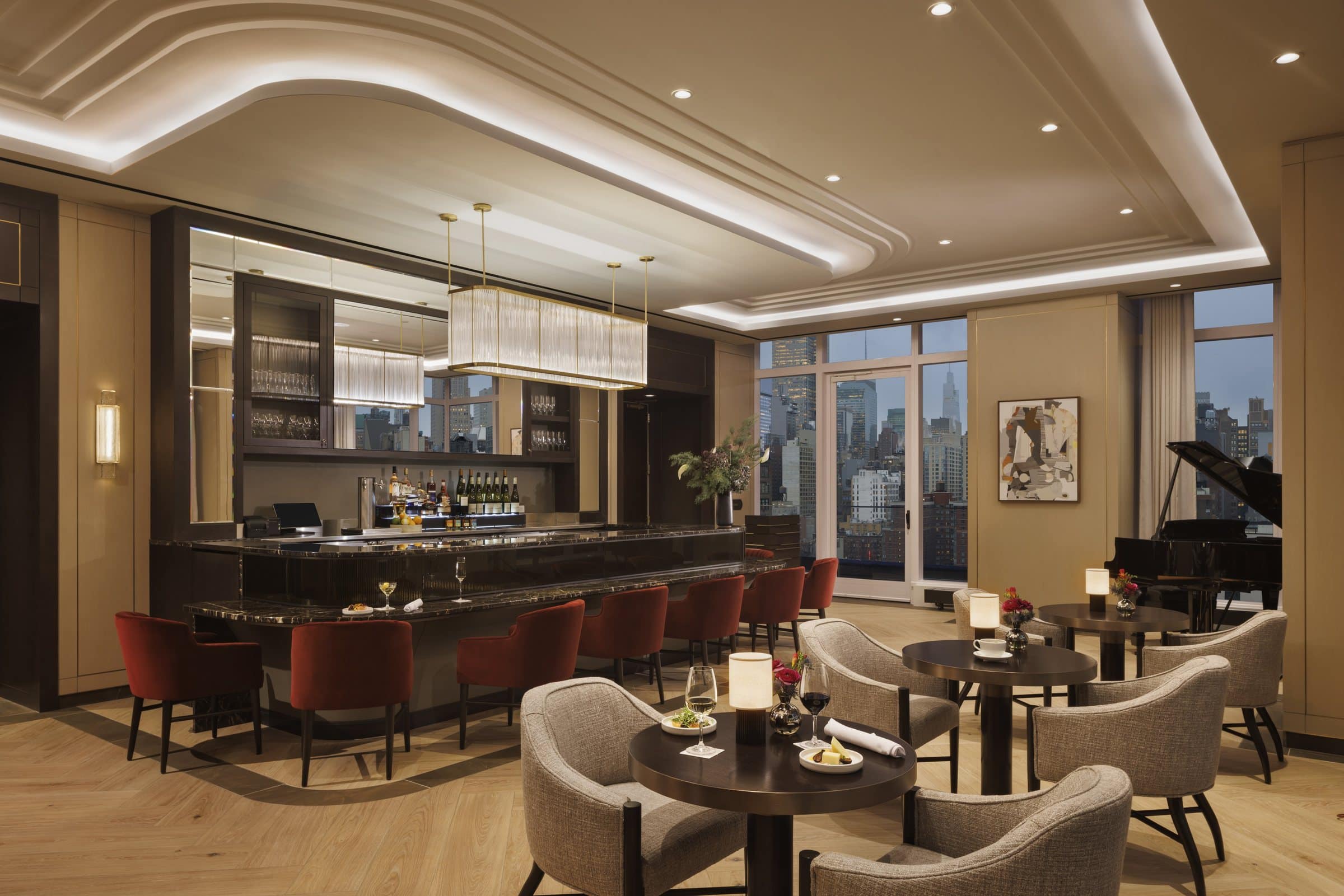 Bar lounge with red chairs, a grand piano and a framed gray, white and rust collage beside the windows