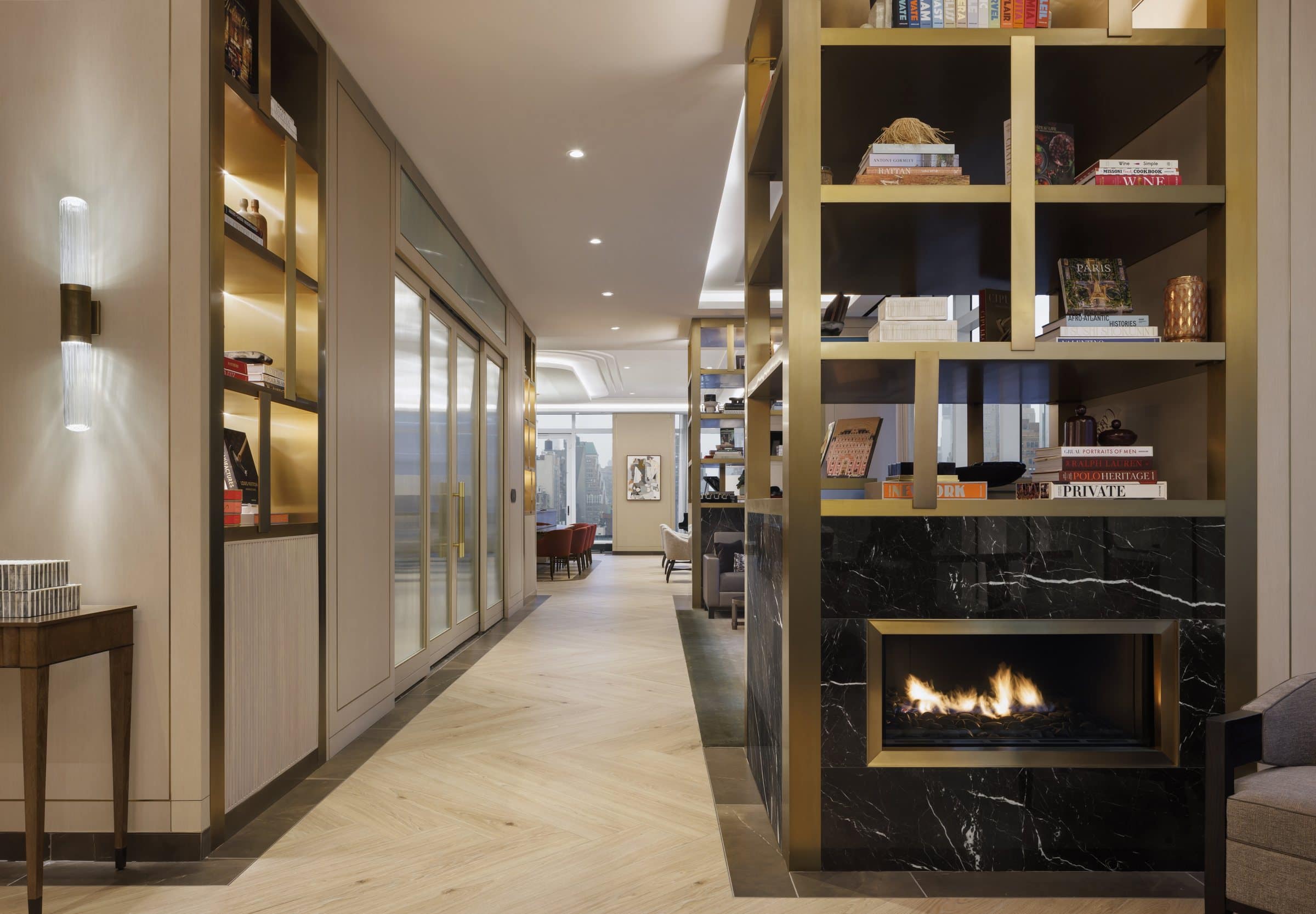 Library corridor beside brass bookshelves and a black marble fireplace, looking toward a small framed collage