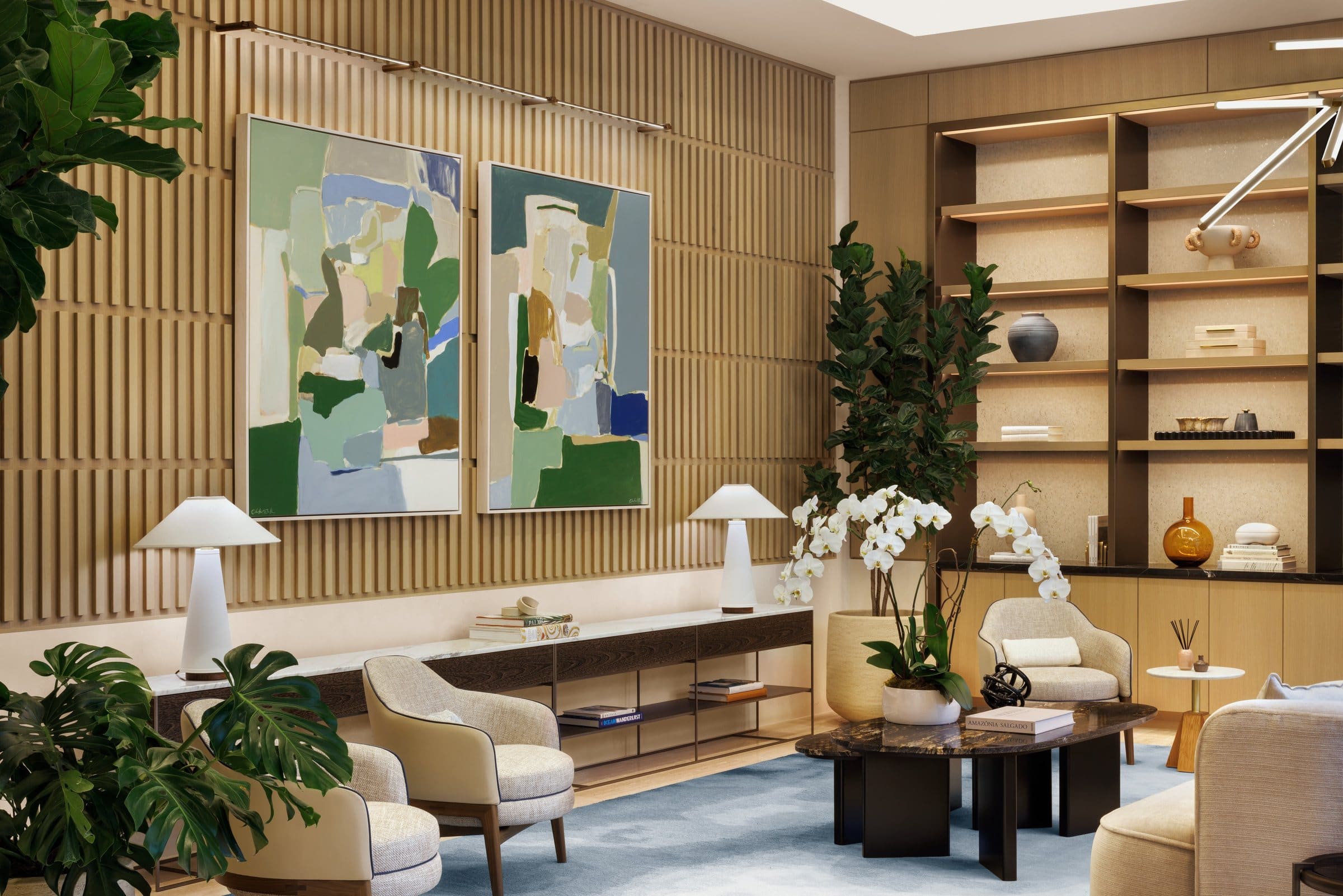 Two green, blue and cream abstract paintings on a slatted wood wall above lounge seating and a console