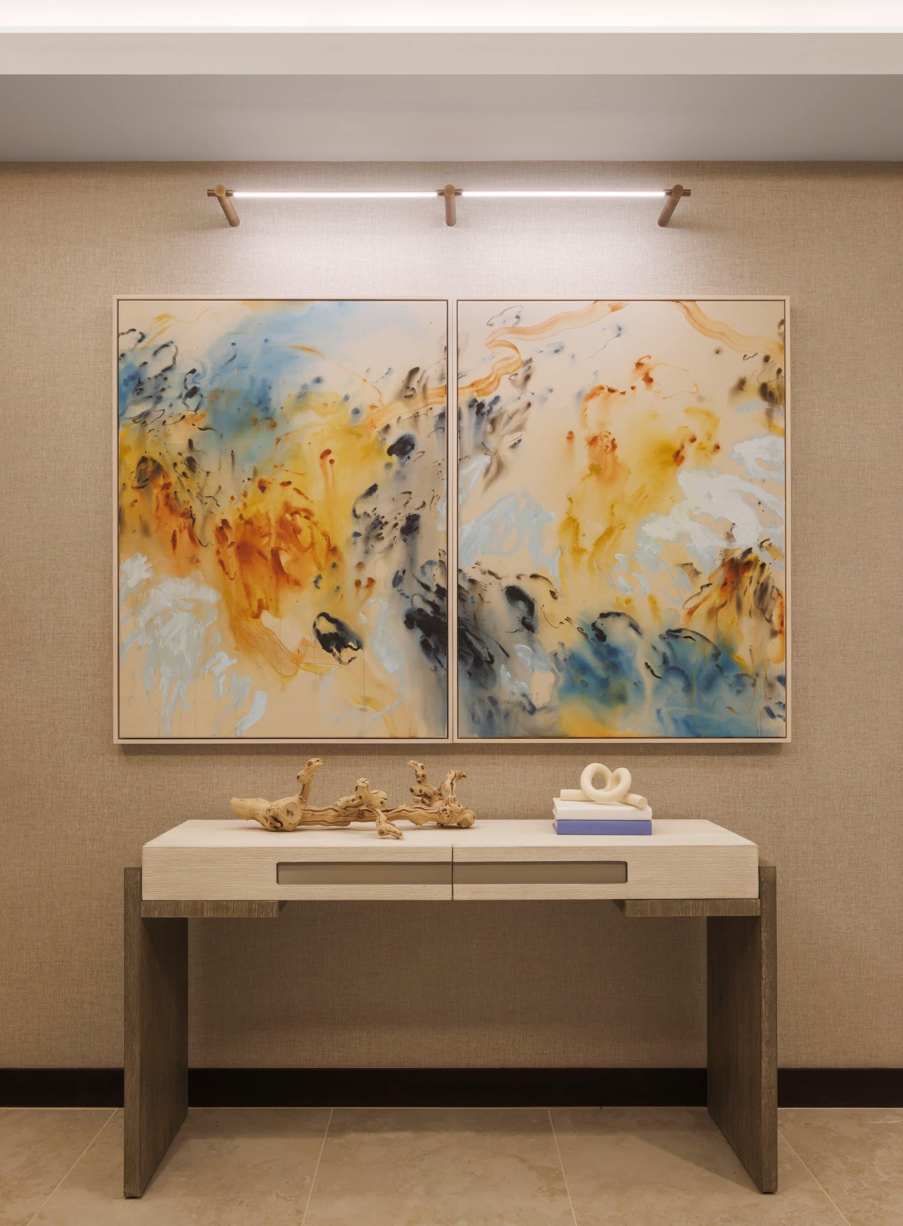 An ochre, pale blue and black abstract diptych above a stone console with driftwood