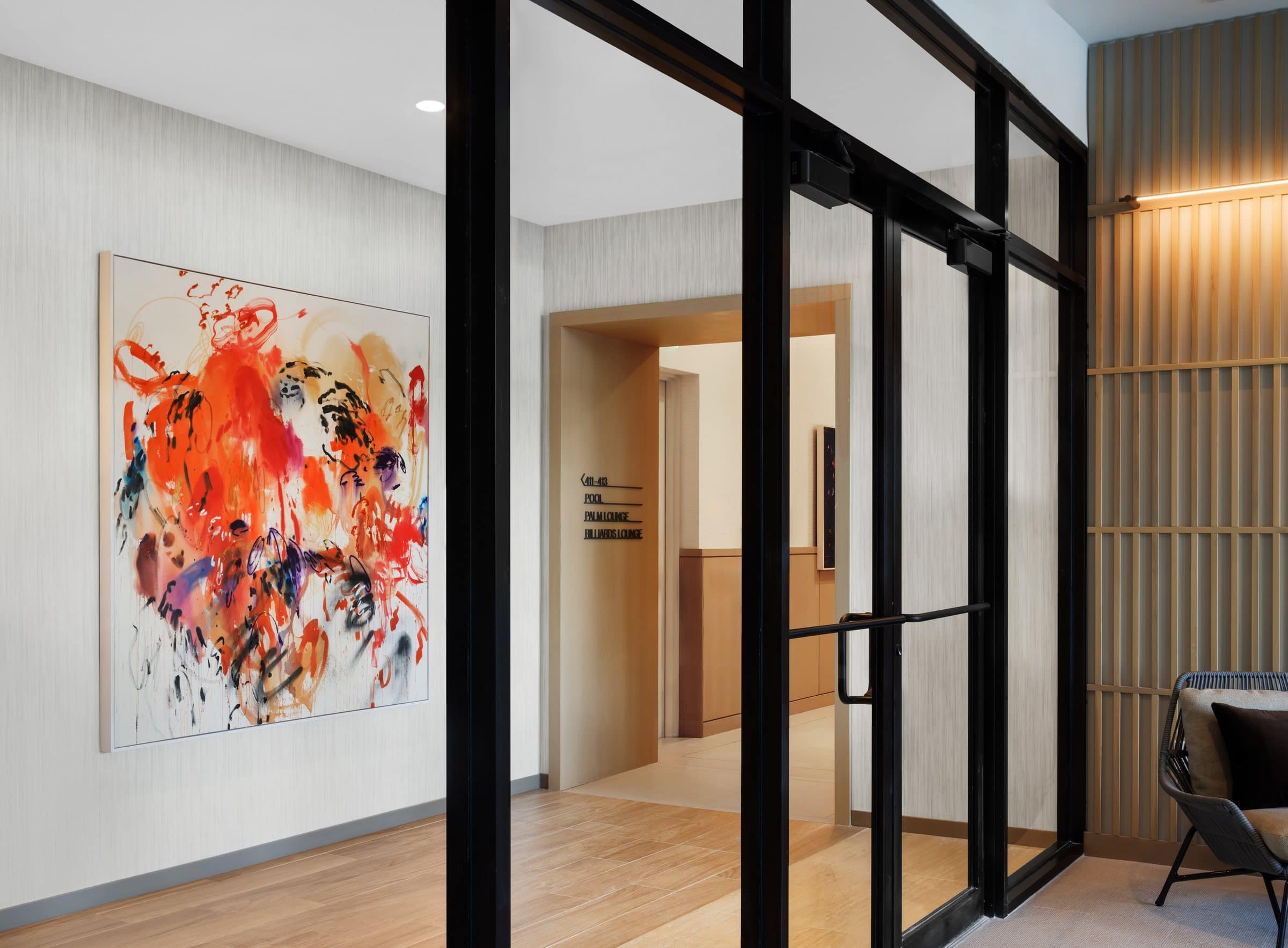 A square red-orange and black gestural painting beside an elevator opening, seen through black-framed glass doors