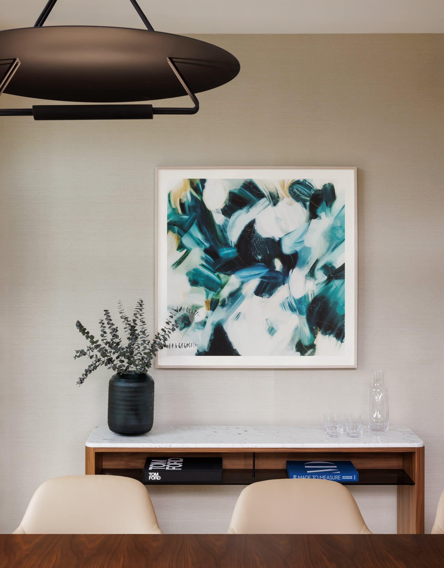A framed teal, green and white gestural print above a console behind a conference table