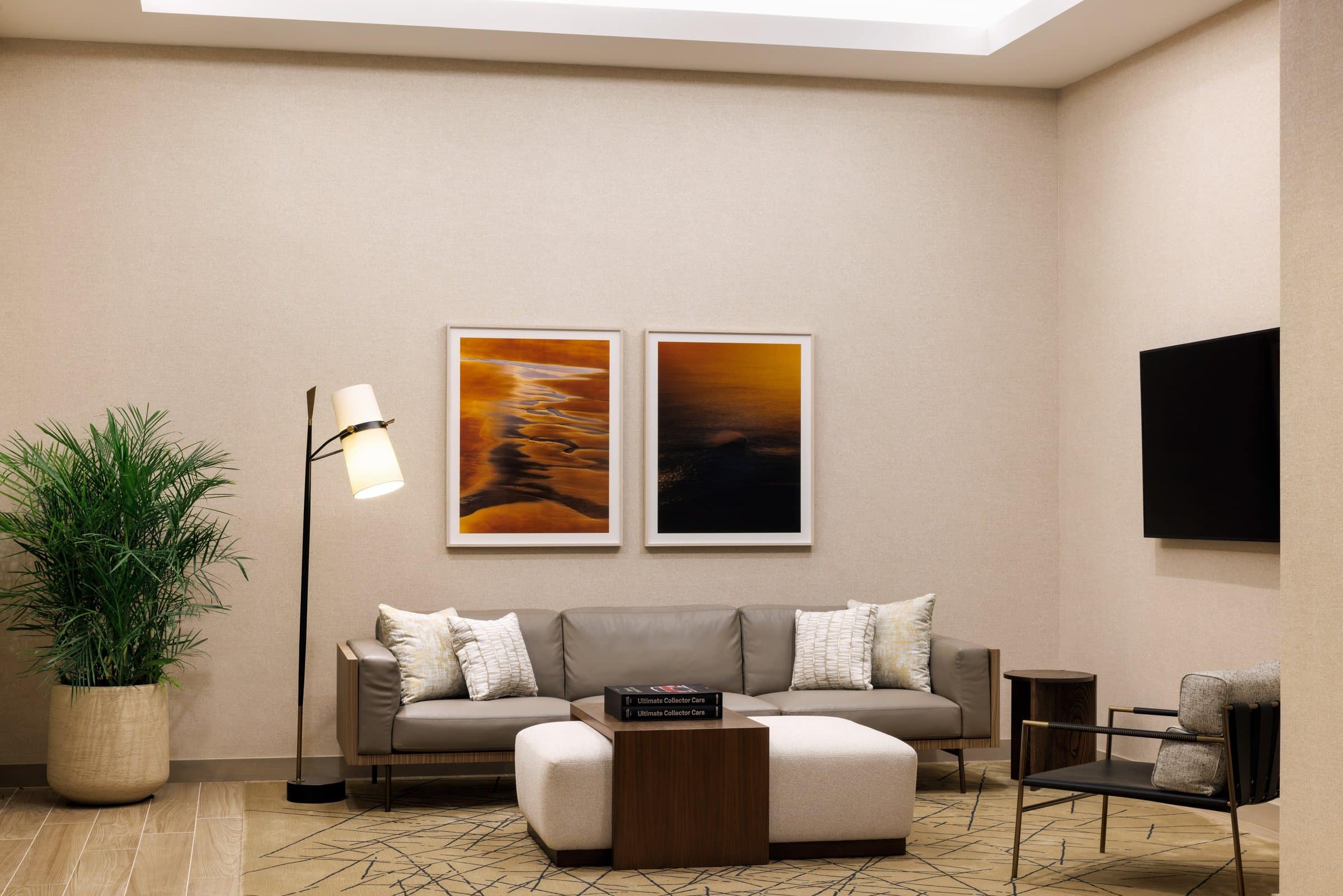 Two gold and dark-blue seascape photographs above a gray sofa in a lounge with a wall-mounted screen