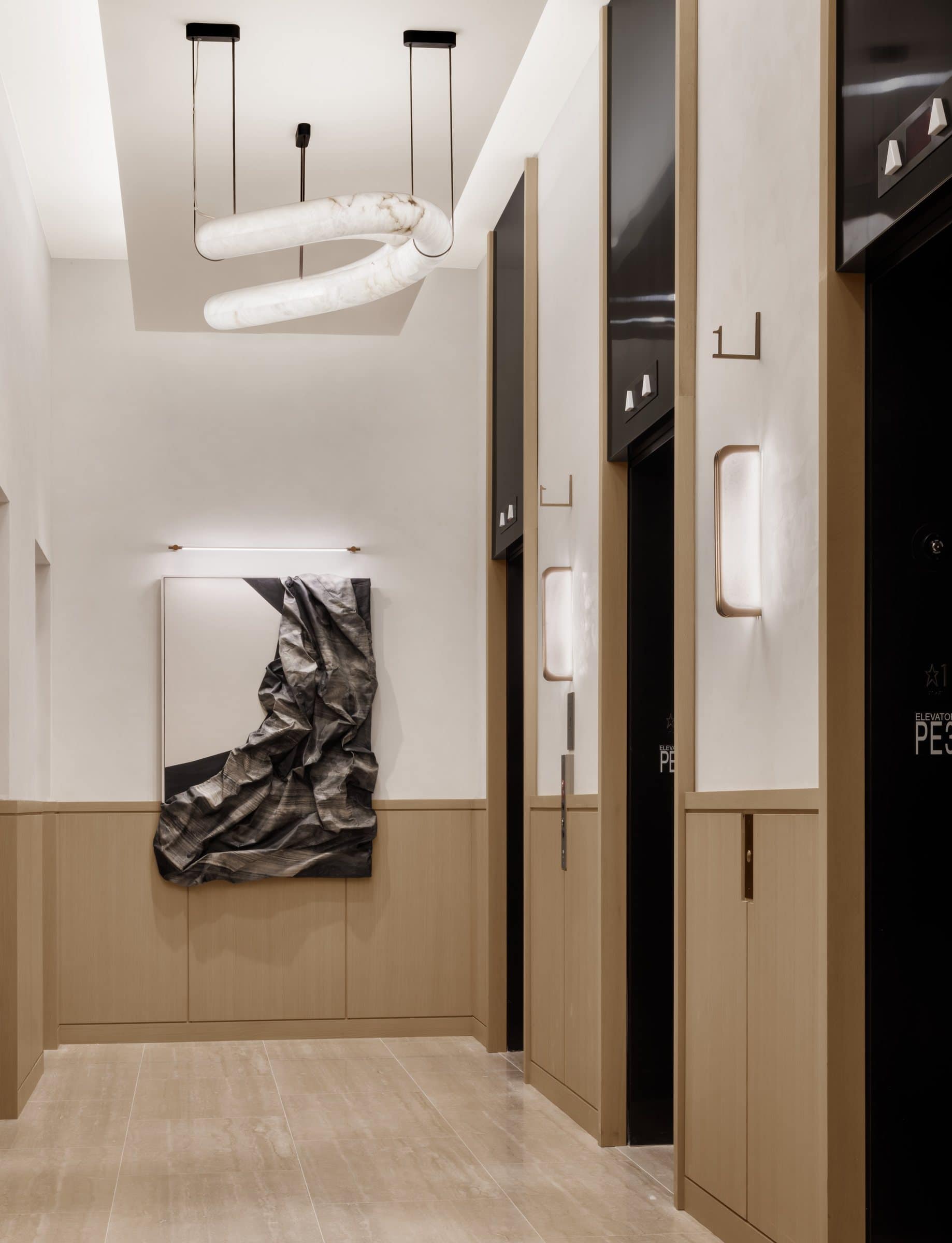 A draped charcoal-gray and white canvas relief at the end of a tall wood-paneled elevator vestibule