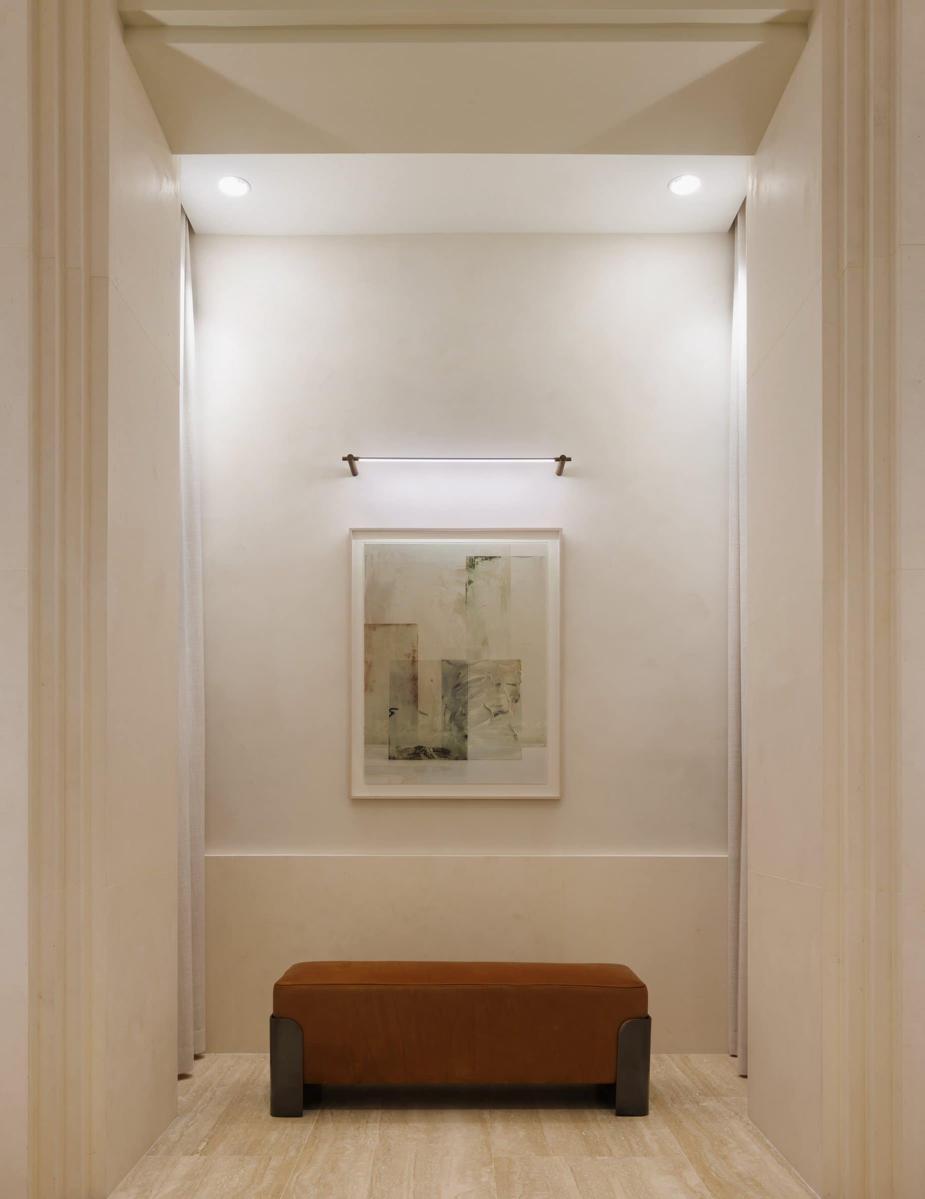 A pale geometric print above a brown upholstered bench in a tall stone-trimmed alcove
