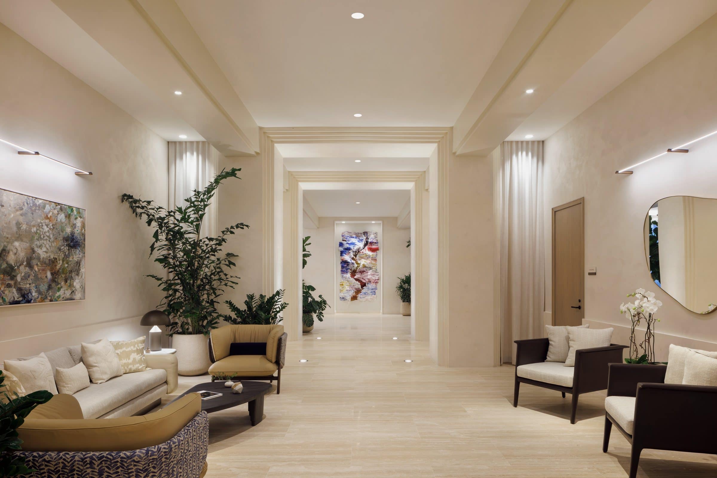 Cream lounge seating beneath a mottled abstract painting, looking down a long hall toward a colorful vertical work
